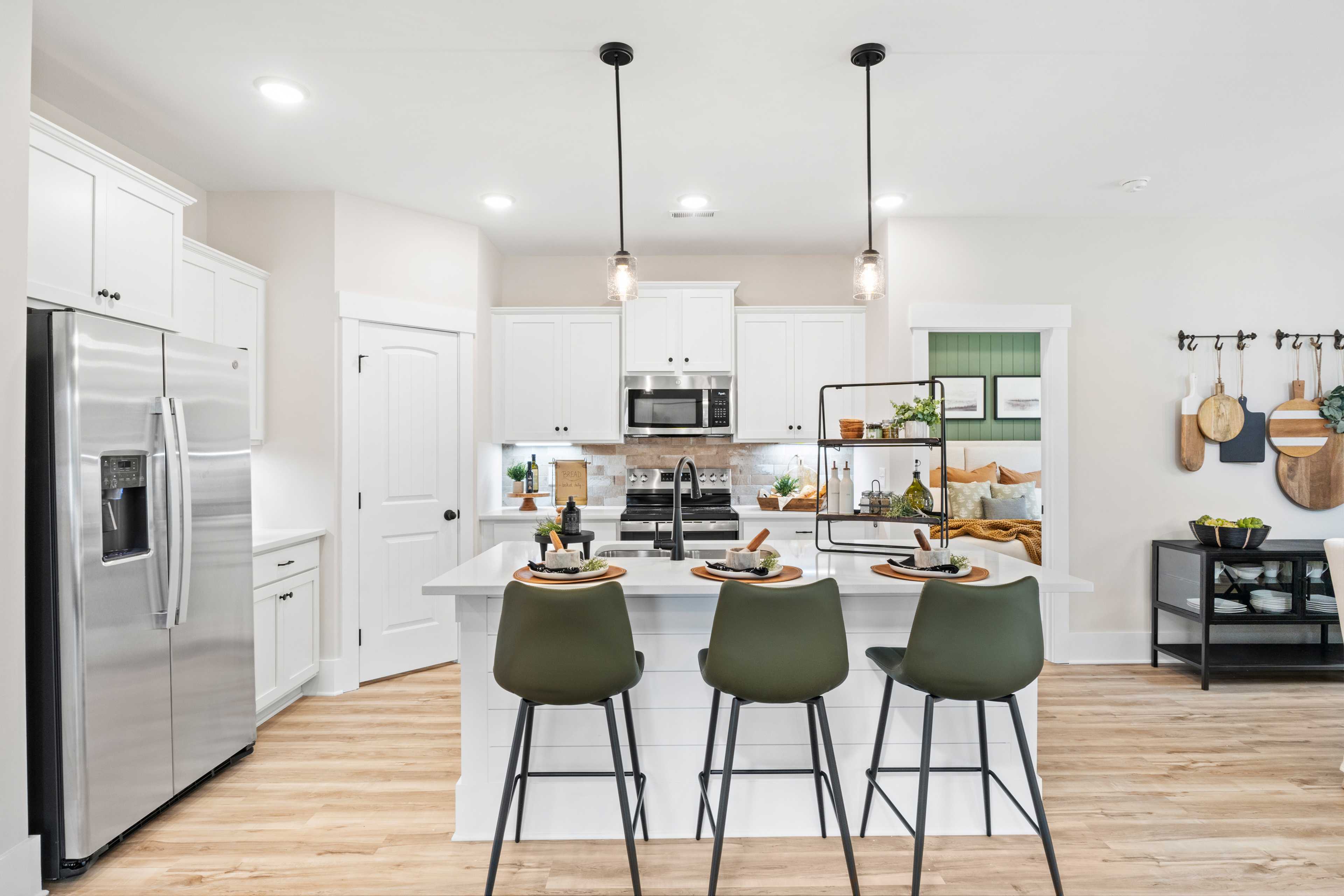 Modern white kitchen in Spragins Cove, Huntsville AL with island bar, green stools, stainless appliances, and hardwood floors