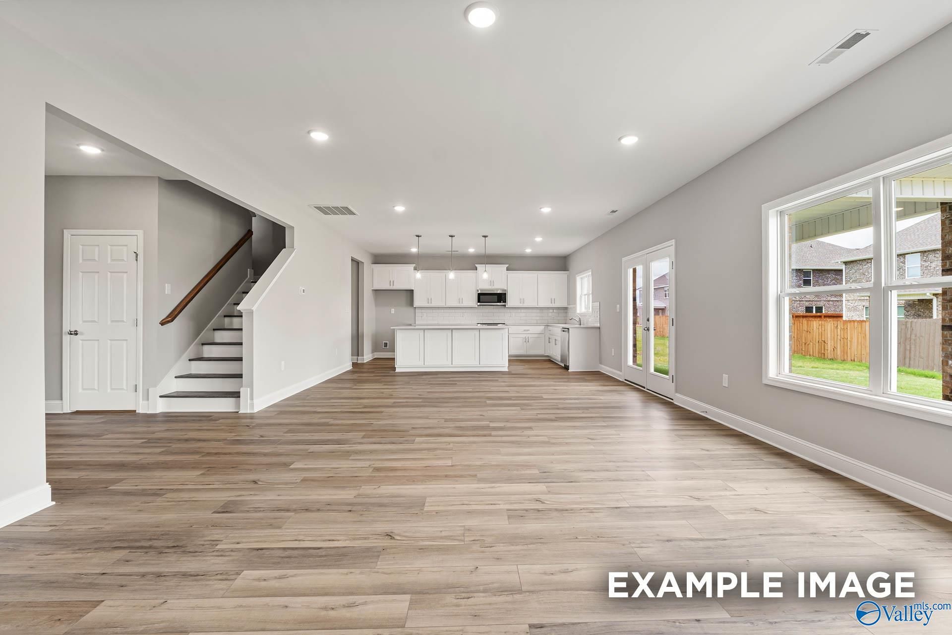 Open-concept living and kitchen with hardwood floors, white cabinetry, island, and staircase in Davidson Homes Chelsea B, Toney, Alabama