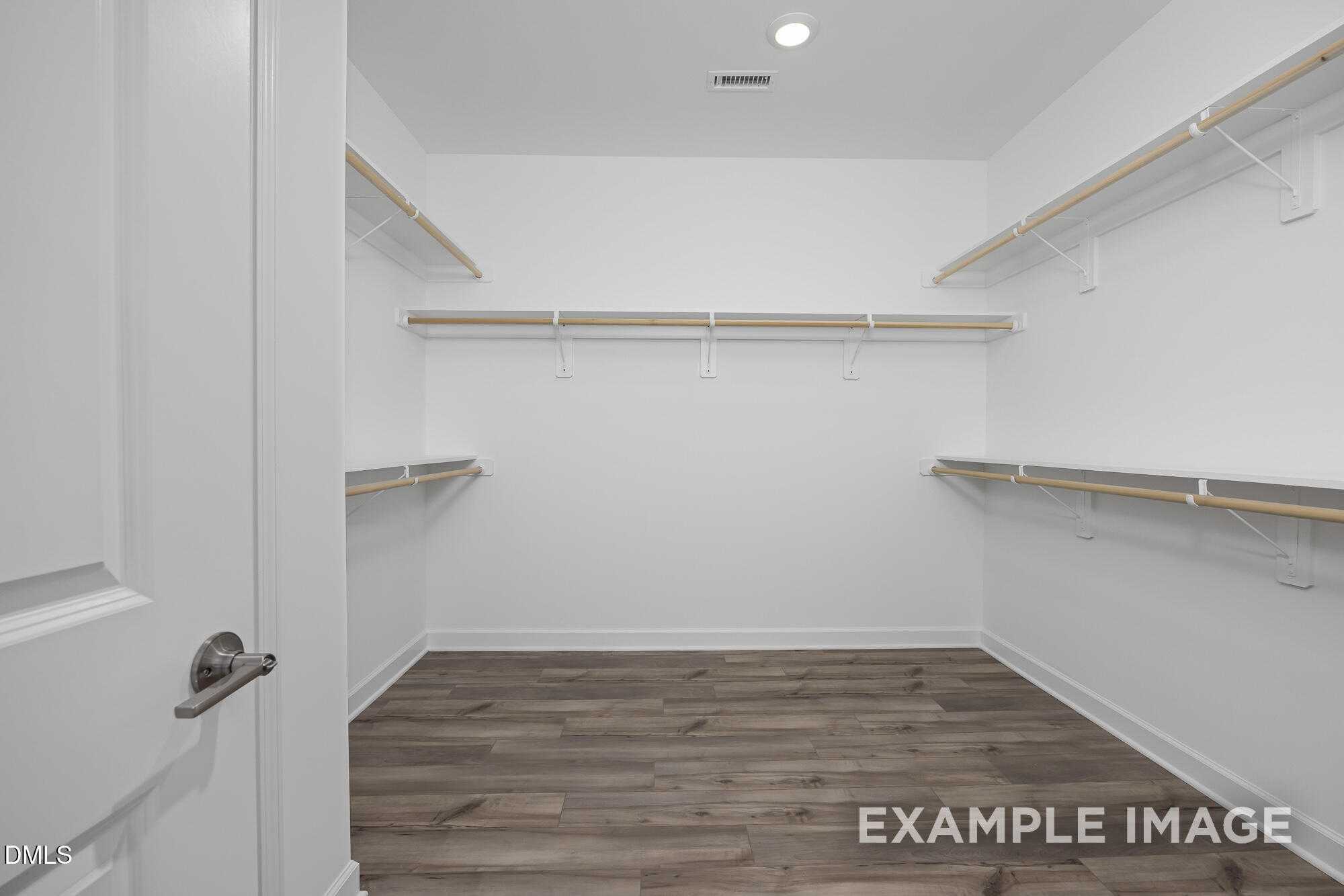 Spacious walk-in closet with white wooden shelving and hardwood floors in Davidson Homes The Cypress B II, Angier, NC