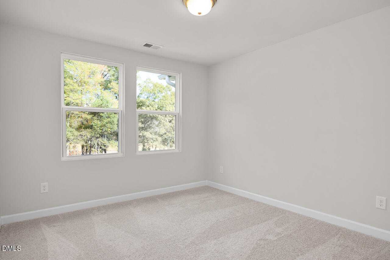 Bright secondary bedroom with large windows overlooking trees, light gray walls, and carpet in Davidson Homes The Warren, Fuquay-Varina, NC