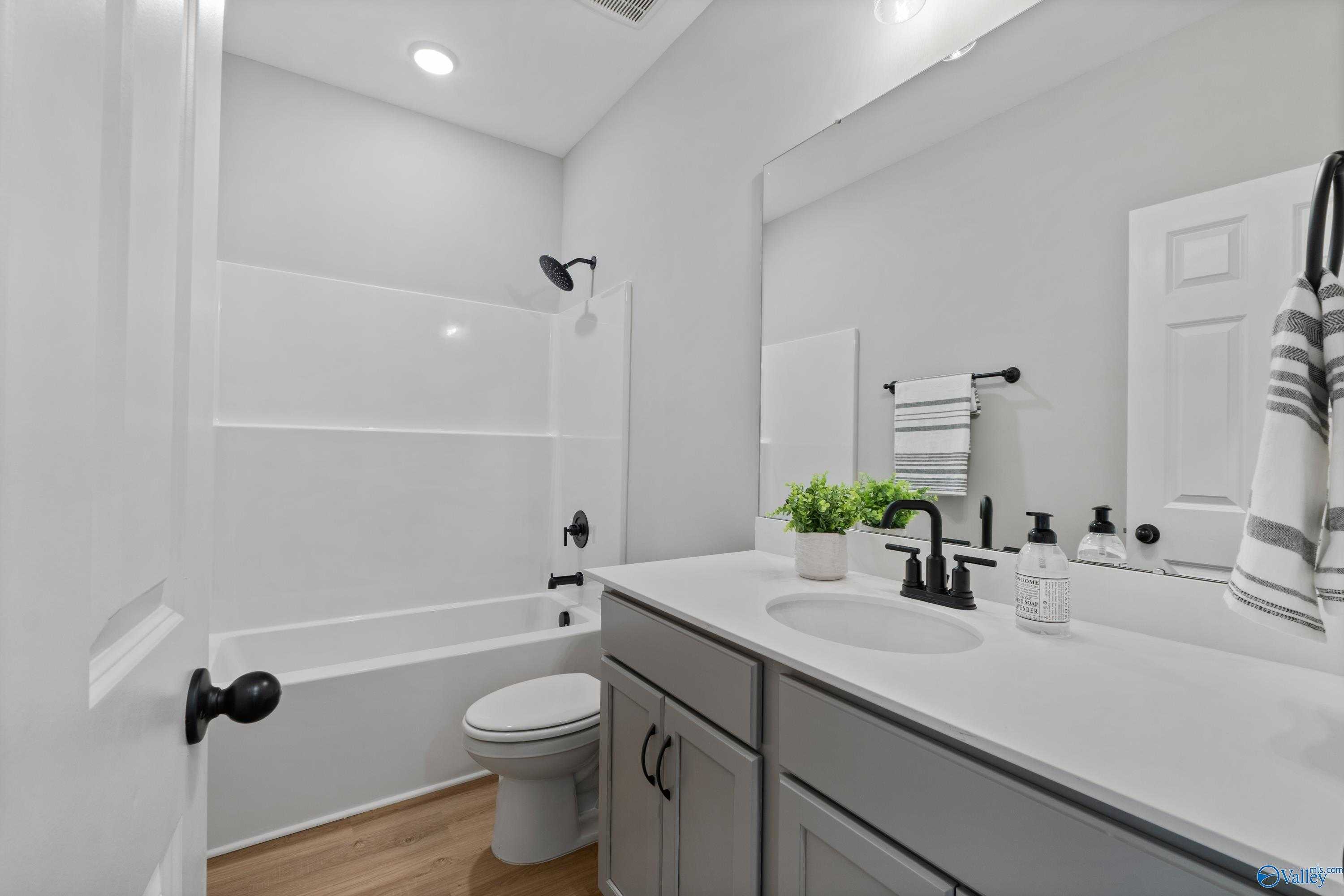 Modern white bathroom with tub-shower combo, gray shaker vanity, large mirror in The Daphne C, Davidson Homes, Owens Cross Roads, AL