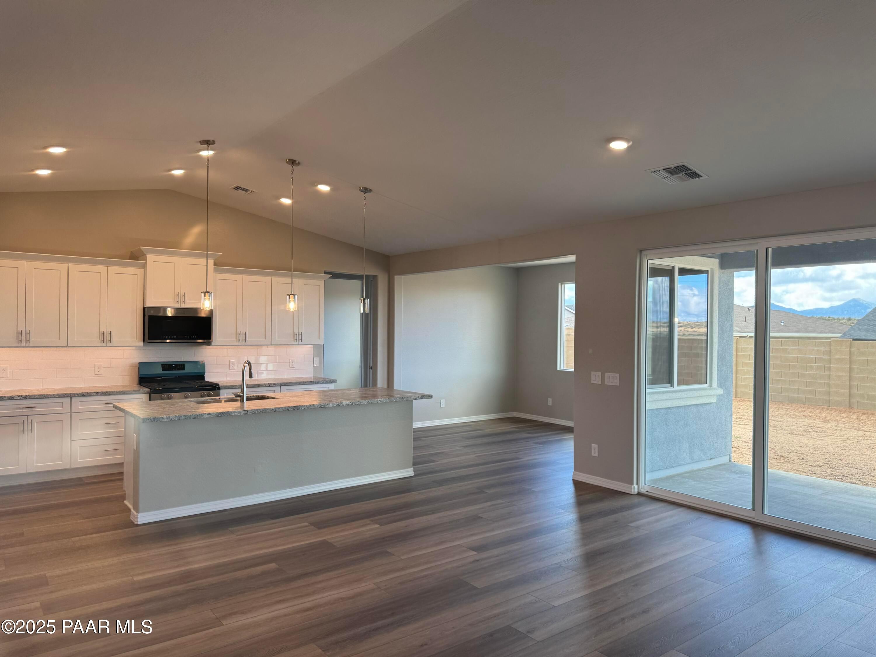 Open-concept kitchen with white cabinets, large island sink, and sliding doors to desert patio in The Monarch A, Prescott, Arizona