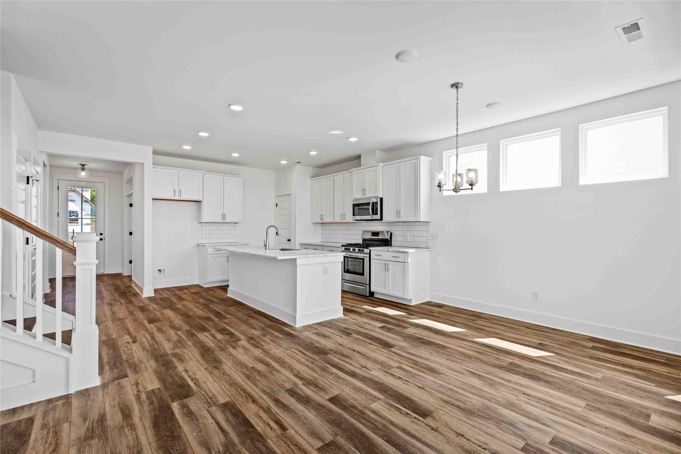 Modern open-concept kitchen with white cabinets, center island, and wood-style flooring in The Ash O floor plan, Heartland.