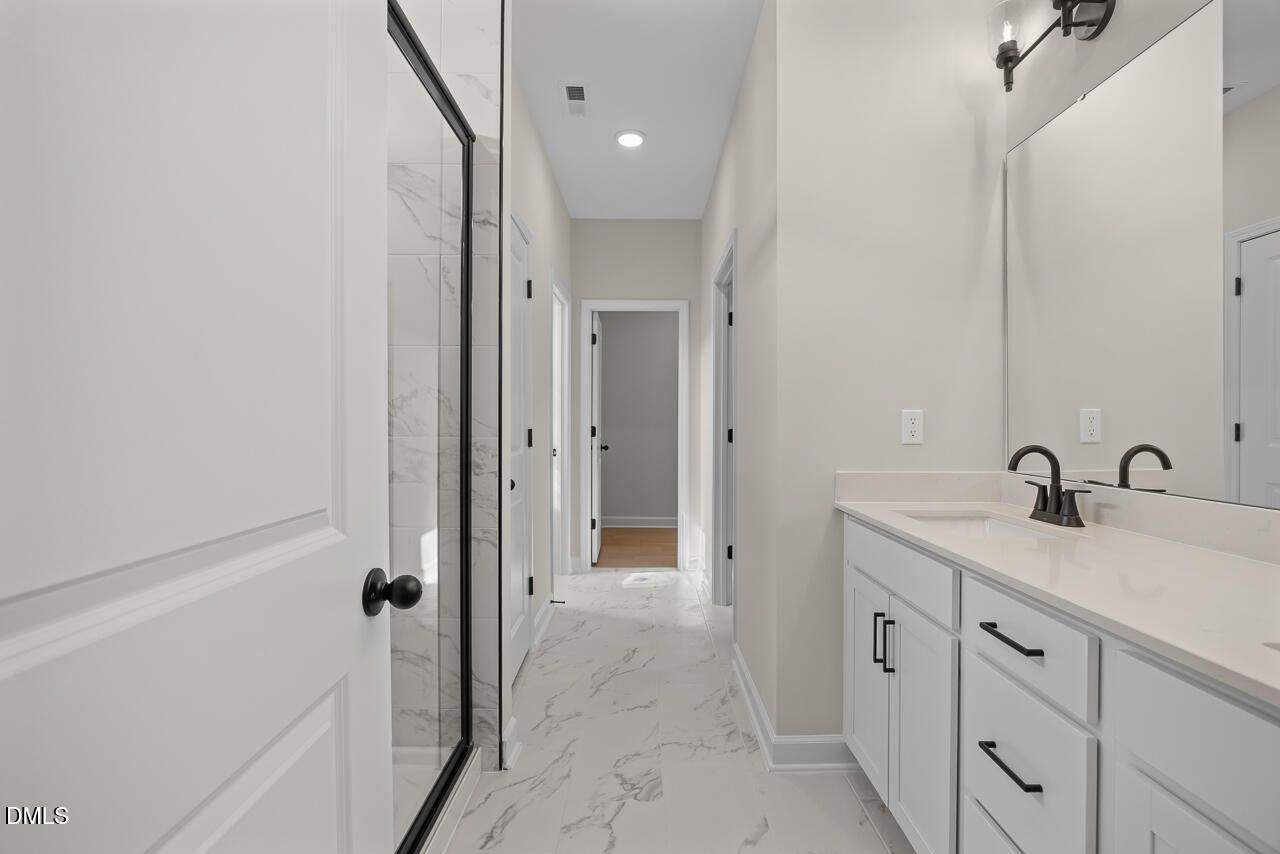 Modern primary bathroom with double vanity, glass walk-in shower, marble tile flooring in The Ashport M plan, Wendell Ridge, NC