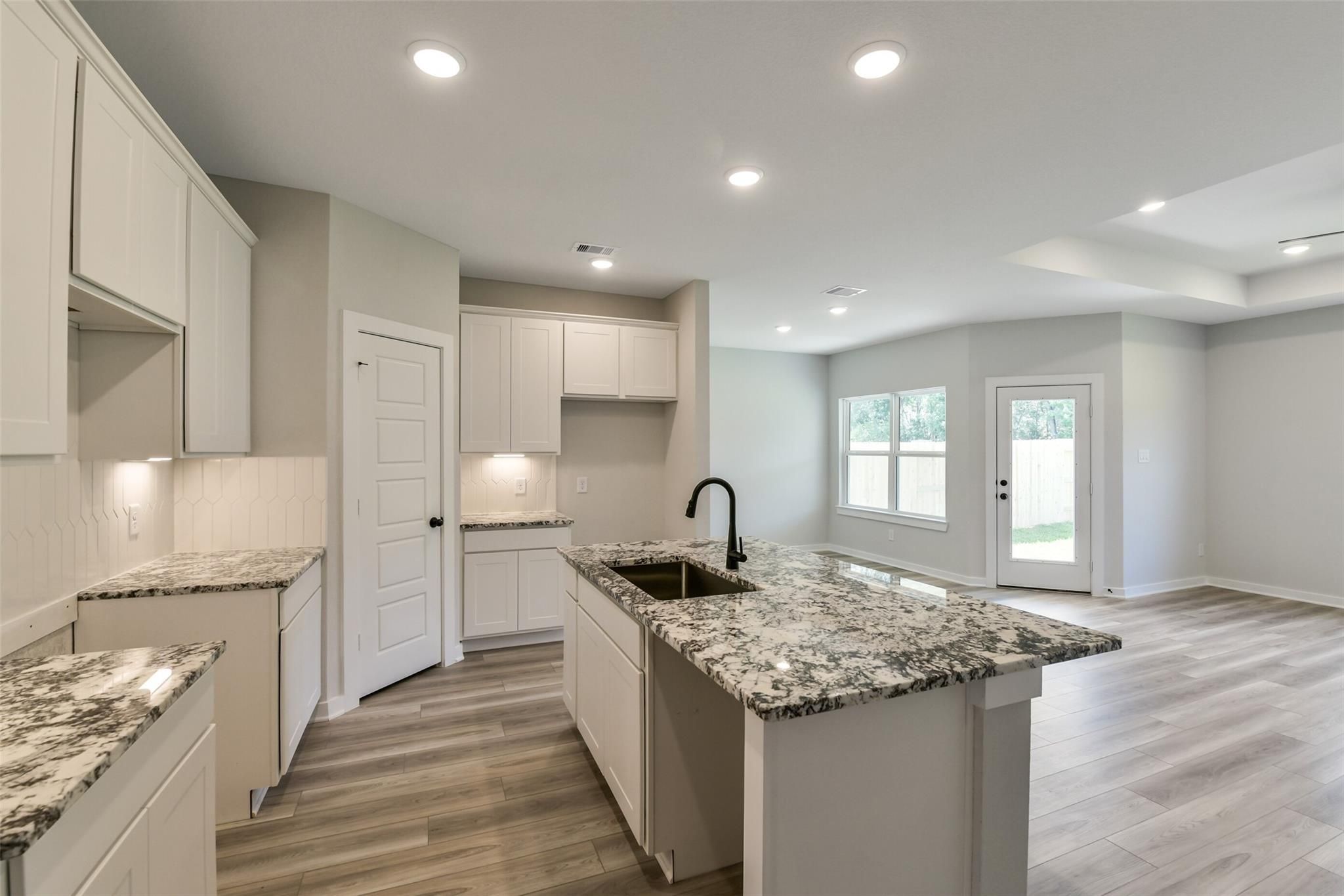 Modern white kitchen with granite island sink and open living area in The Daphne H 4-bedroom home, Crosby, Texas