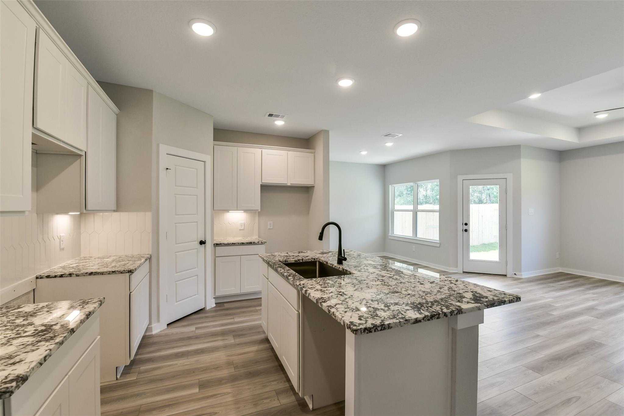 Modern white kitchen with granite island sink and open living area in The Daphne H 4-bedroom home, Crosby, Texas