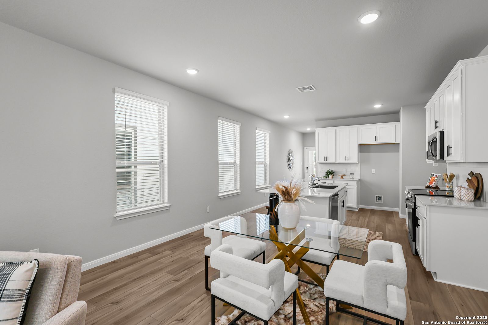 Elegant open dining area with glass table, white chairs, and adjacent white kitchen in Davidson Homes The Gillian C, San Antonio, Texas