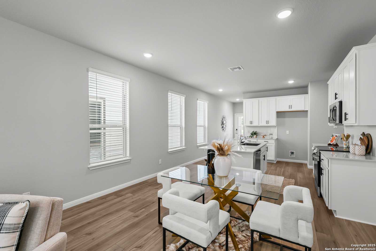 Elegant open dining area with glass table, white chairs, and adjacent white kitchen in Davidson Homes The Gillian C, San Antonio, Texas