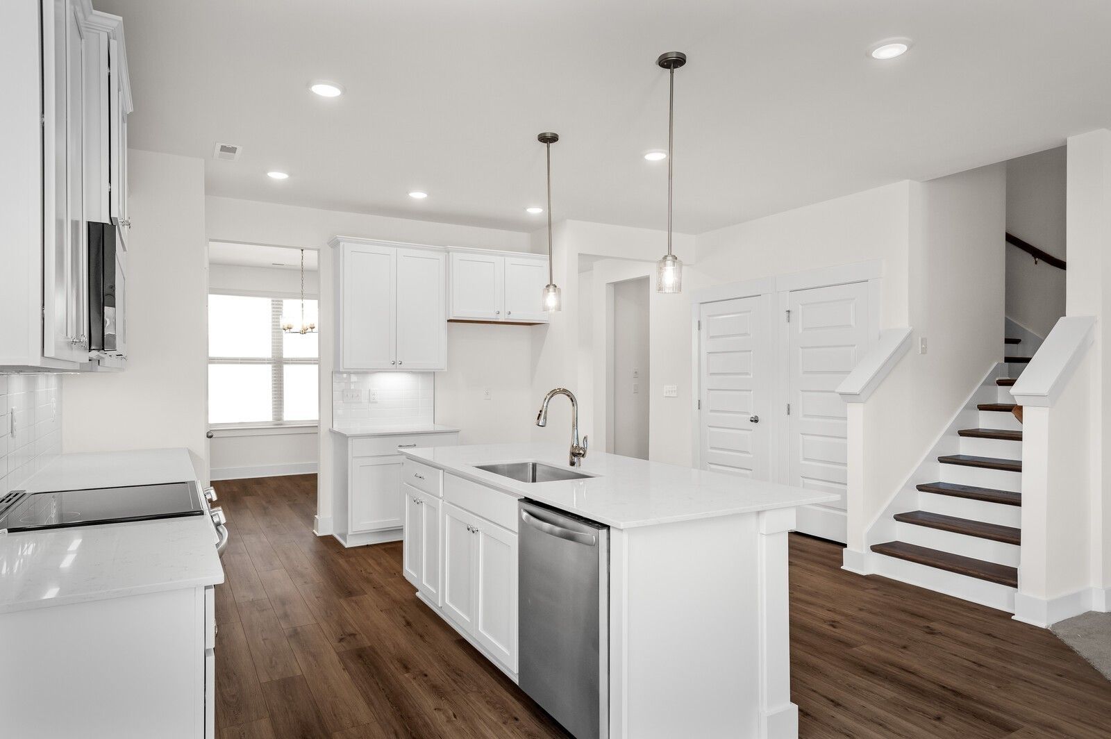 Modern white kitchen with island, stainless appliances, and wood flooring in The Ash A floor plan at Woods Crossing, Gallatin.