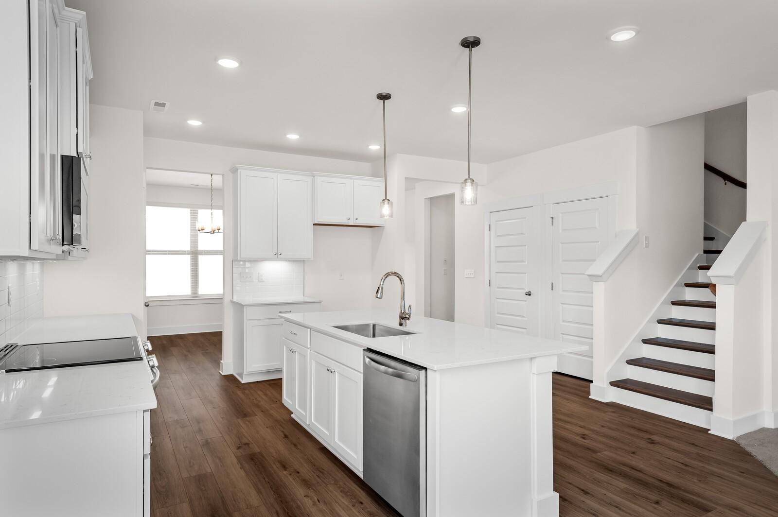 Modern white kitchen with island, stainless appliances, and wood flooring in The Ash A floor plan at Woods Crossing, Gallatin.
