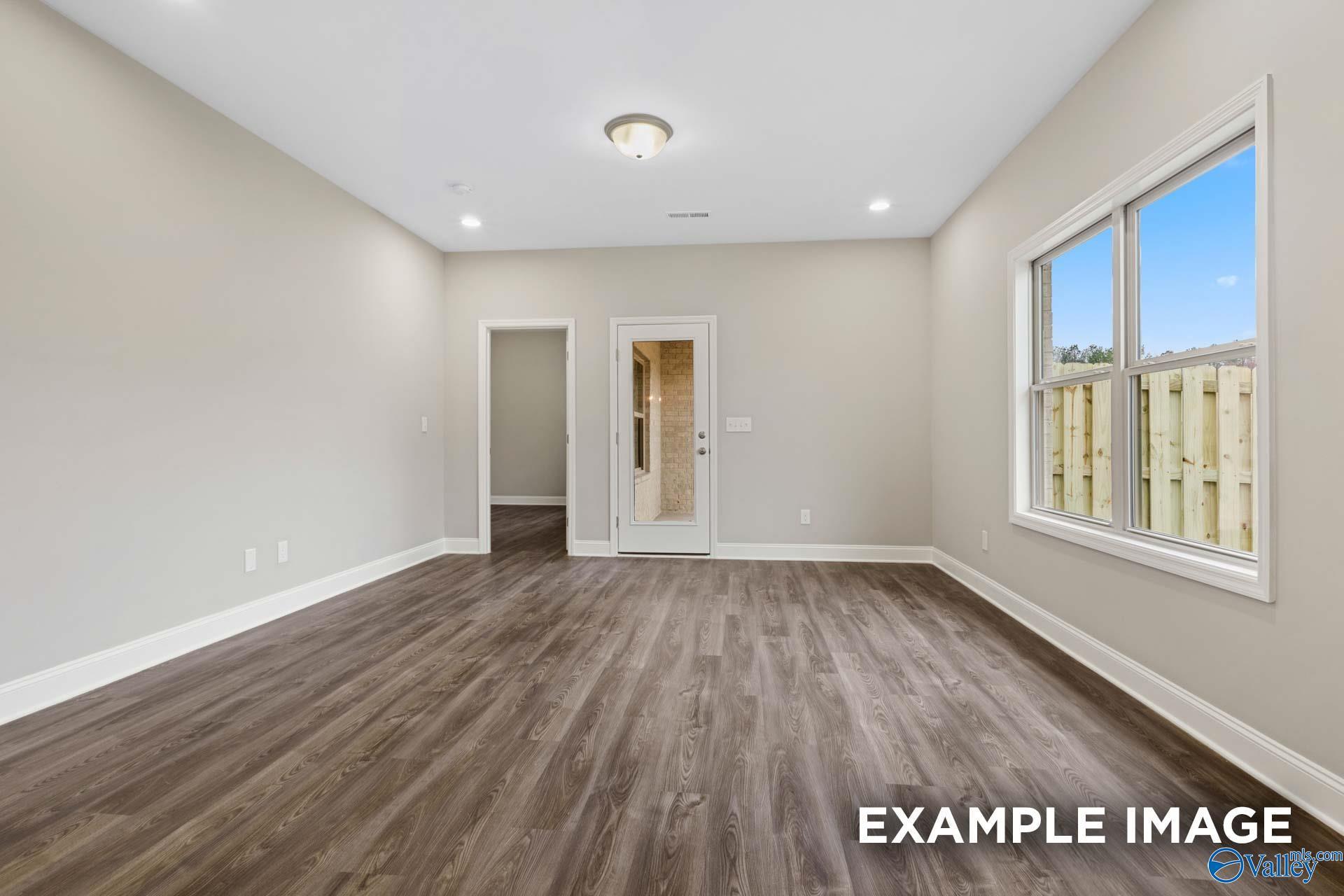 Spacious bedroom with hardwood floors, beige walls, and large windows to backyard in Davidson Homes The Camilla A, Hartselle, Alabama