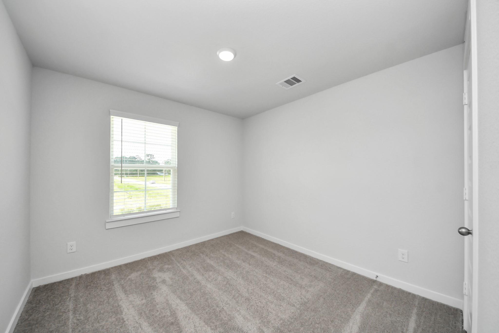 Bright, carpeted bedroom with neutral walls in The Brazos F floor plan at Liberty Estates, Cleveland, Texas.