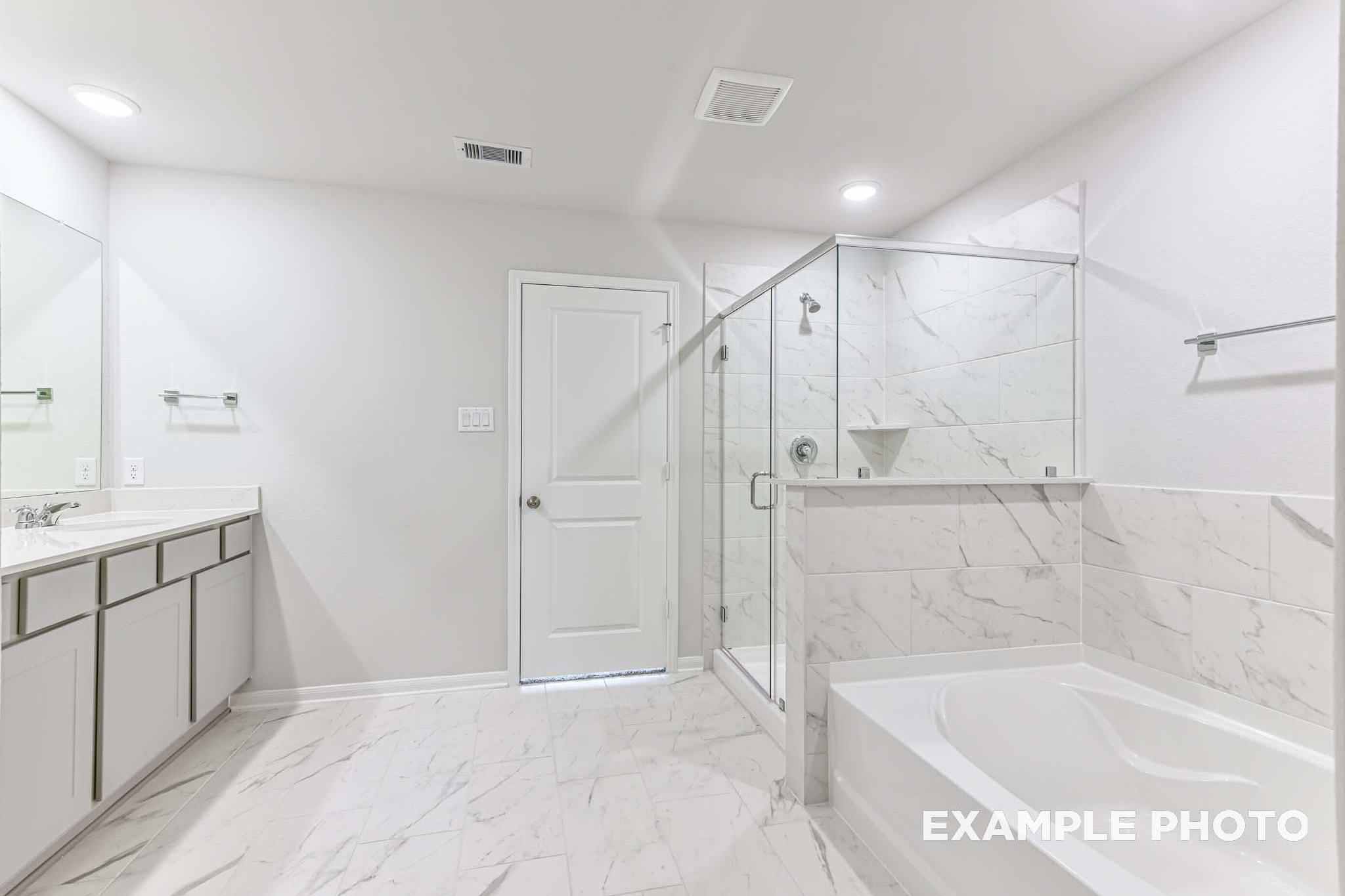 Spacious master bathroom in The Laguna A with white marble tiles, double vanity, freestanding tub, and glass shower
