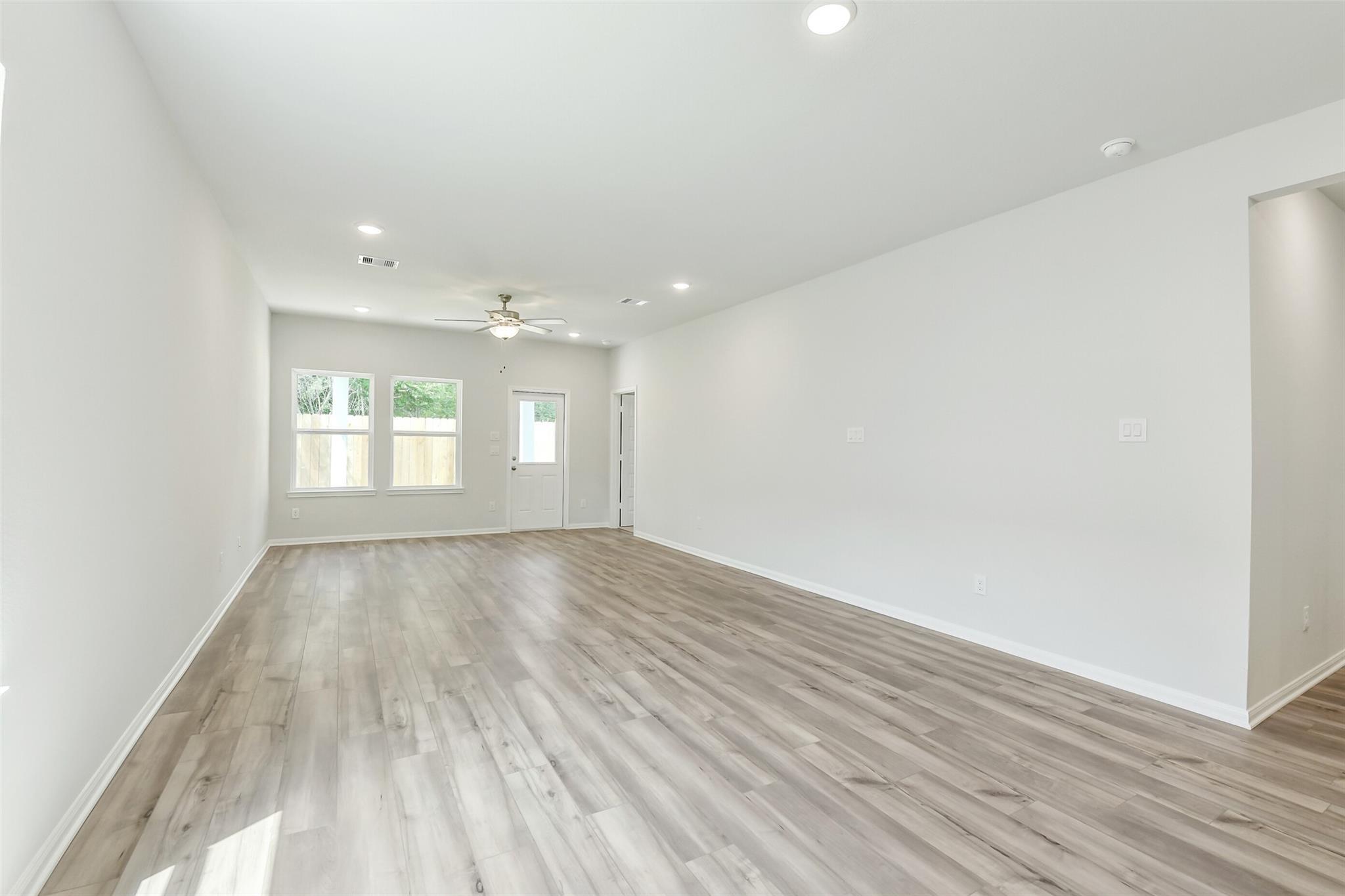 Spacious empty living room with light hardwood floors, large windows, and ceiling fan in Davidson Homes Sabine E, Conroe, Texas