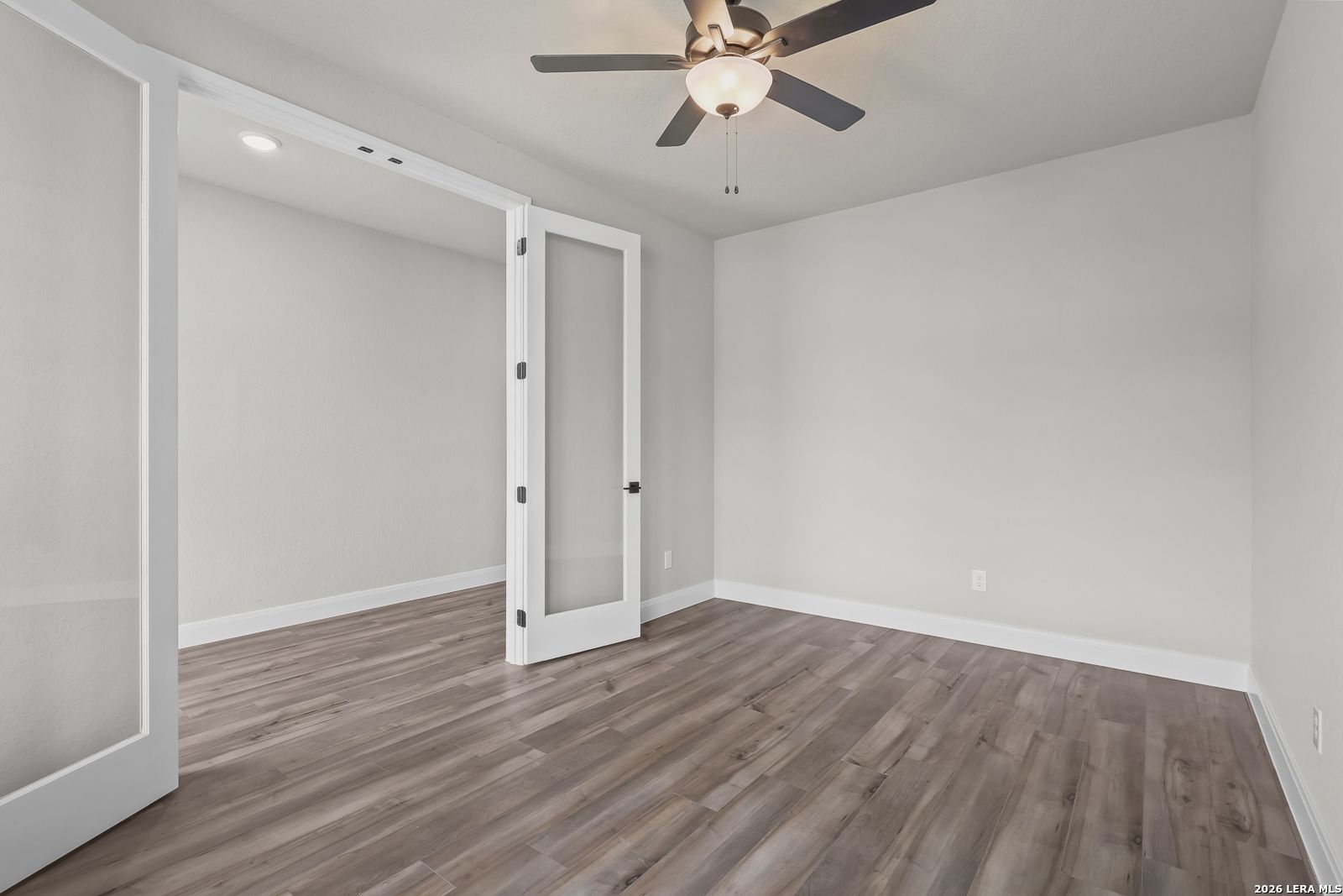 Empty study with open French doors, ceiling fan, light gray walls, and hardwood floors in Davidson Homes The Belmont H, Castroville, Texas