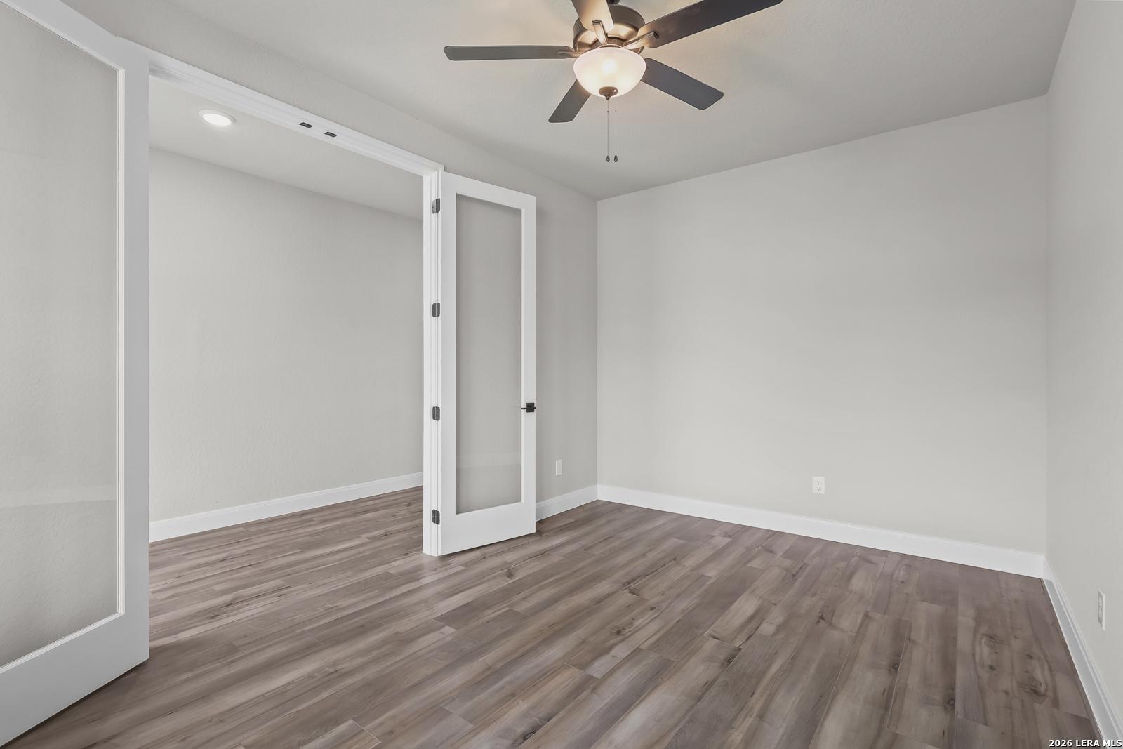 Empty study with open French doors, ceiling fan, light gray walls, and hardwood floors in Davidson Homes The Belmont H, Castroville, Texas