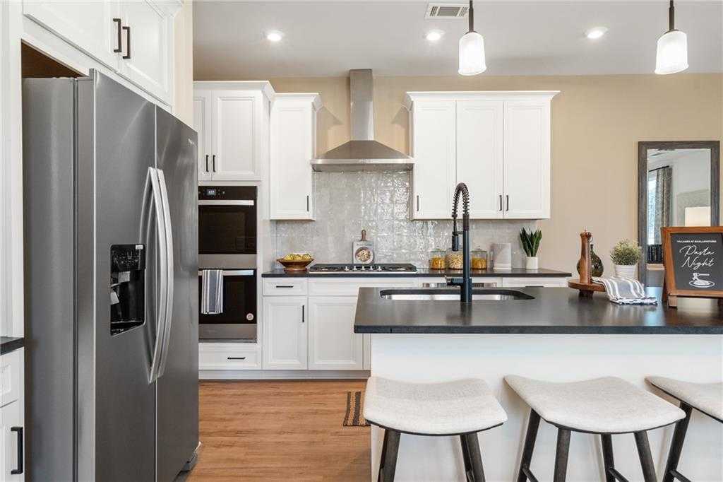 Modern white kitchen with stainless steel appliances, island sink, and bar stools in Davidson Homes The Marion C, Winder, GA