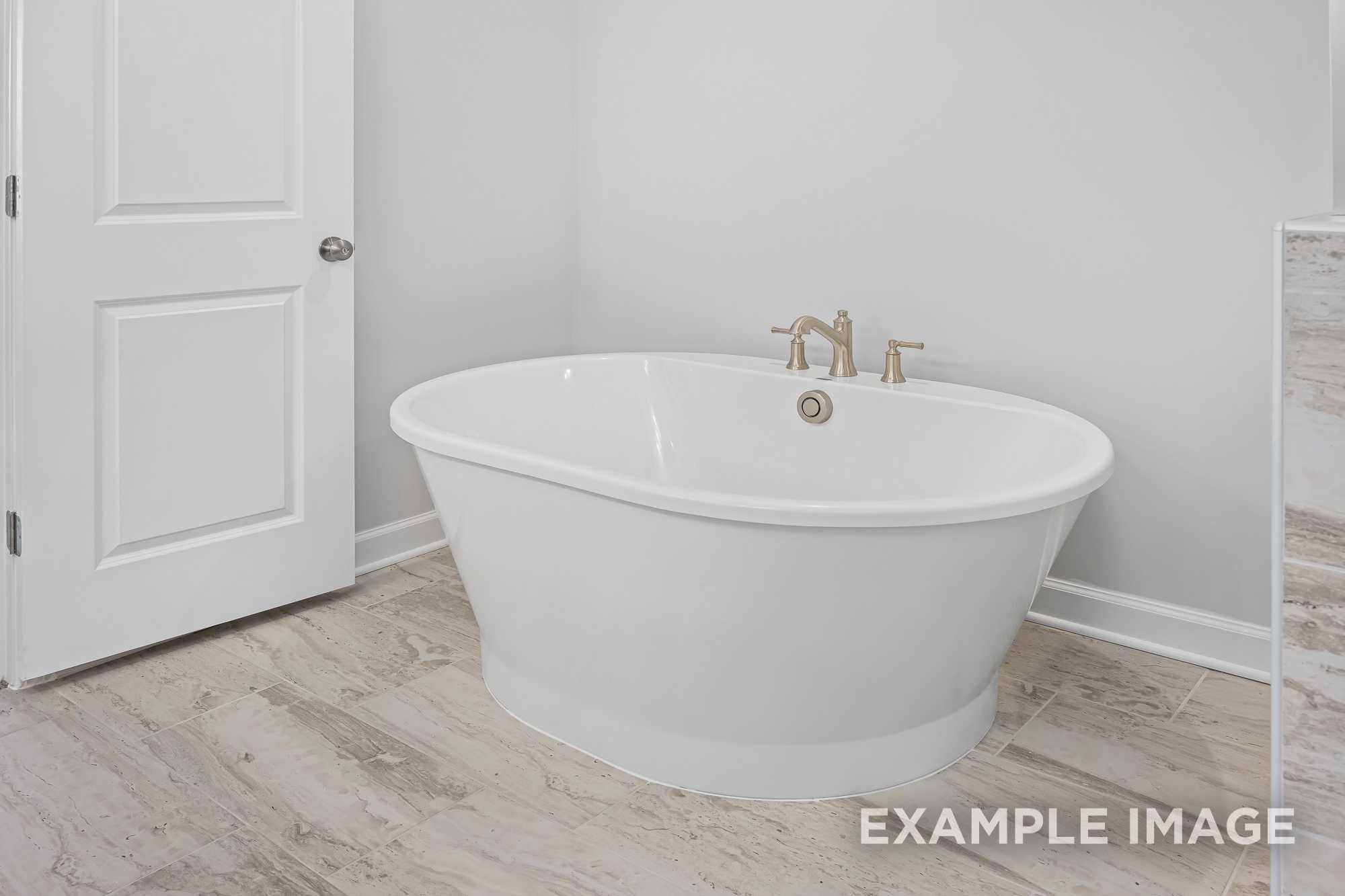 Elegant master bathroom in The Cypress D II featuring freestanding white oval tub, brass faucets, and light wood flooring