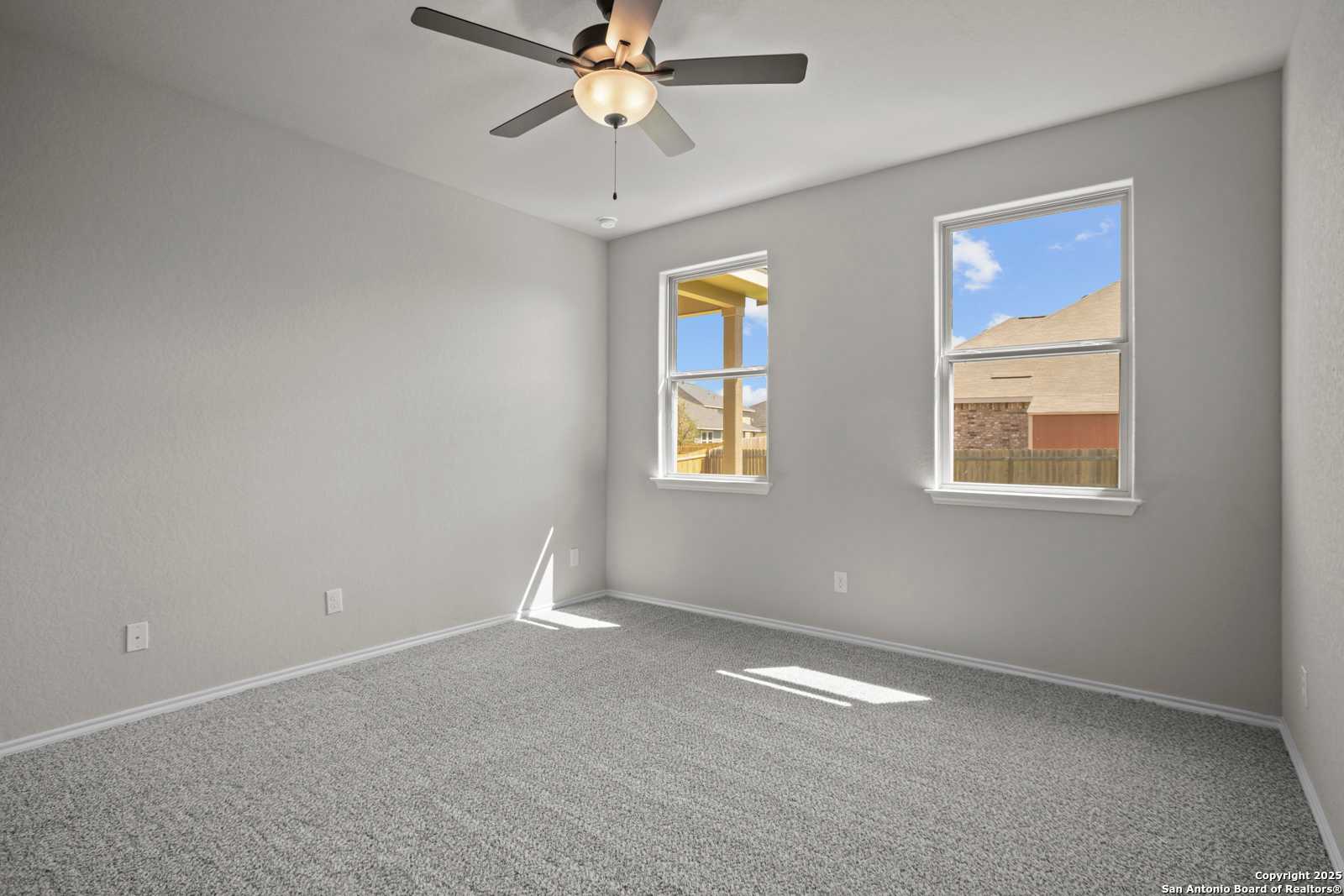 Bright secondary bedroom with gray walls, beige carpet, ceiling fan, and windows overlooking patio in Davidson Homes The Asheville E, Converse, Texas