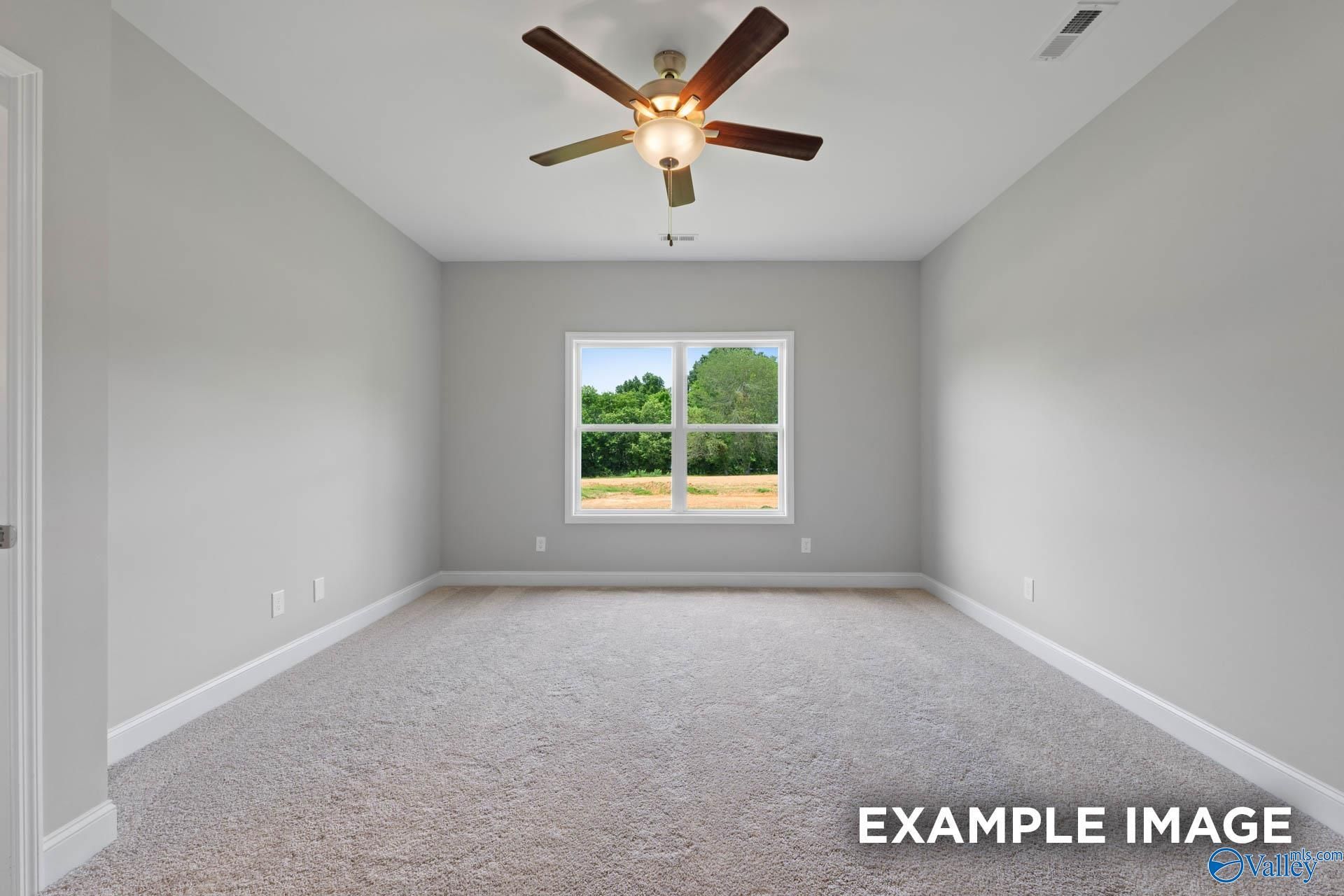 Bright empty bedroom with gray walls, beige carpet, ceiling fan, and large window overlooking trees in The Everett home, Meridianville, Alabama