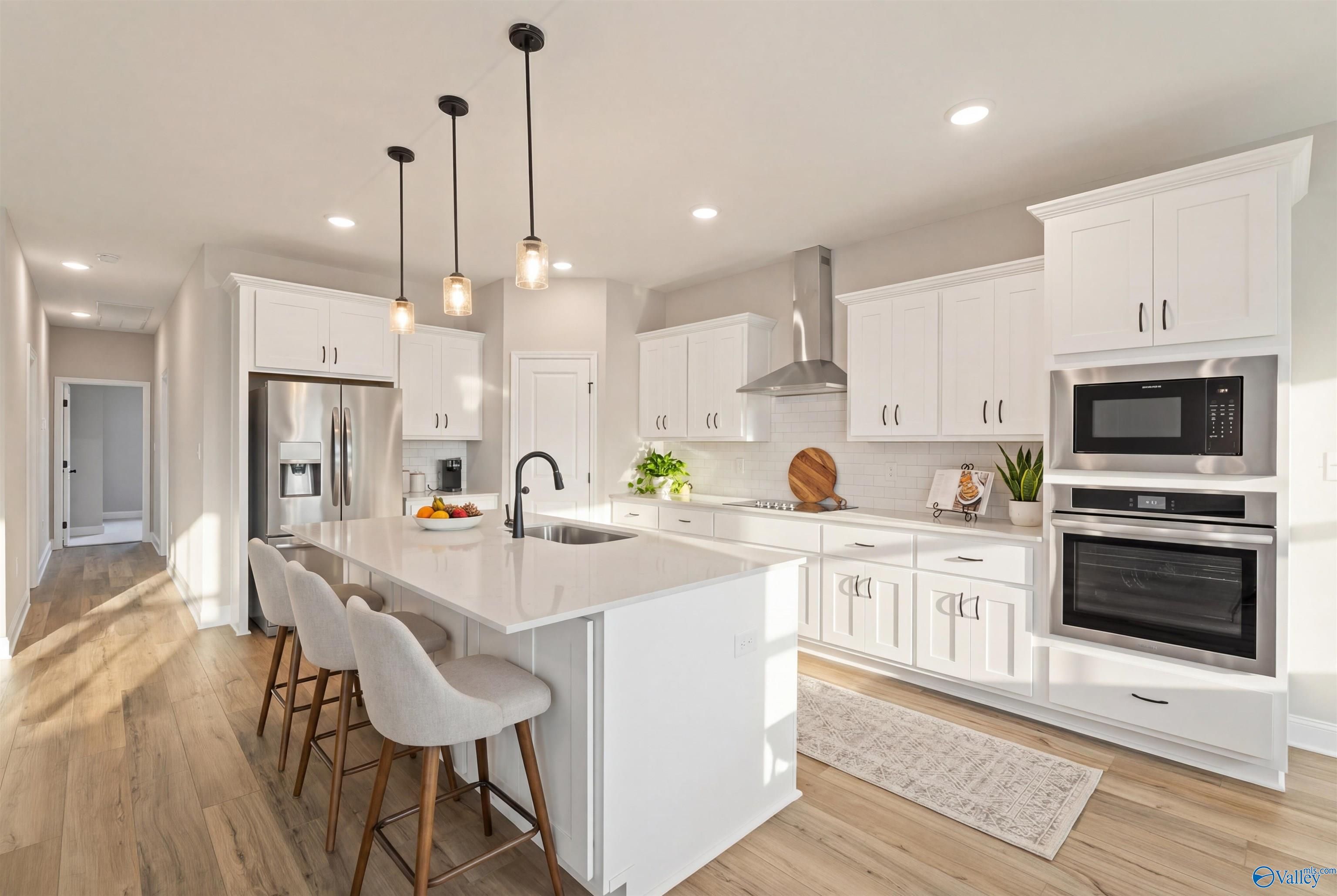 Modern white kitchen island with bar stools, stainless appliances, and pendant lights in Davidson Homes The Rockford with Bonus, Toney, Alabama