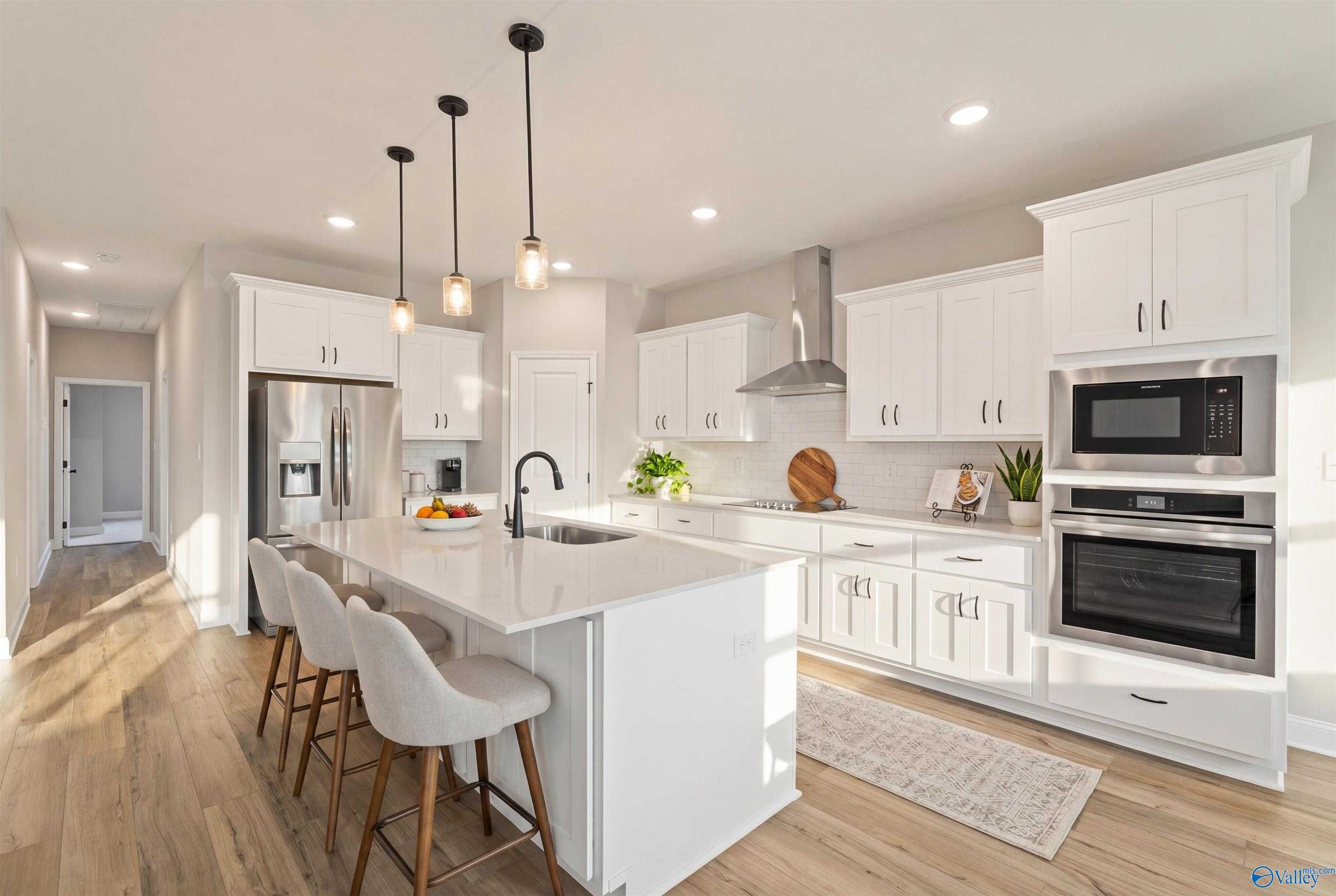 Modern white kitchen island with bar stools, stainless appliances, and pendant lights in Davidson Homes The Rockford with Bonus, Toney, Alabama