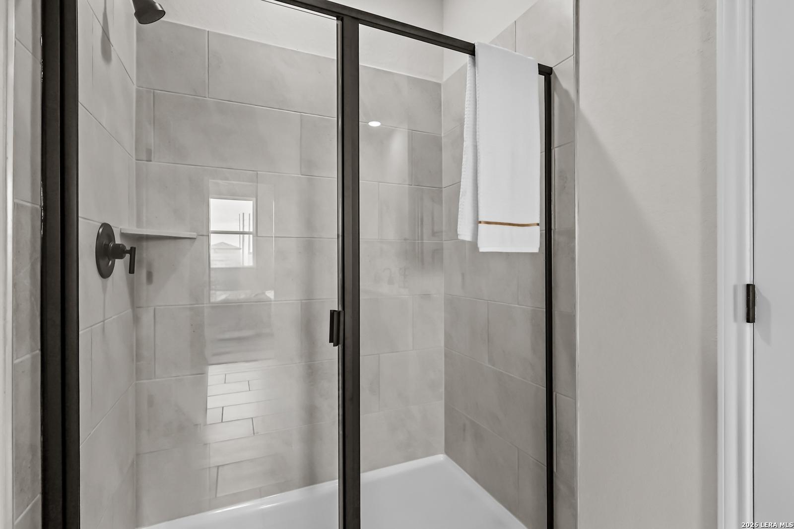 Walk-in shower with modern tile surround and black frame glass door in The Douglas C floor plan, Hannah Heights, Seguin.