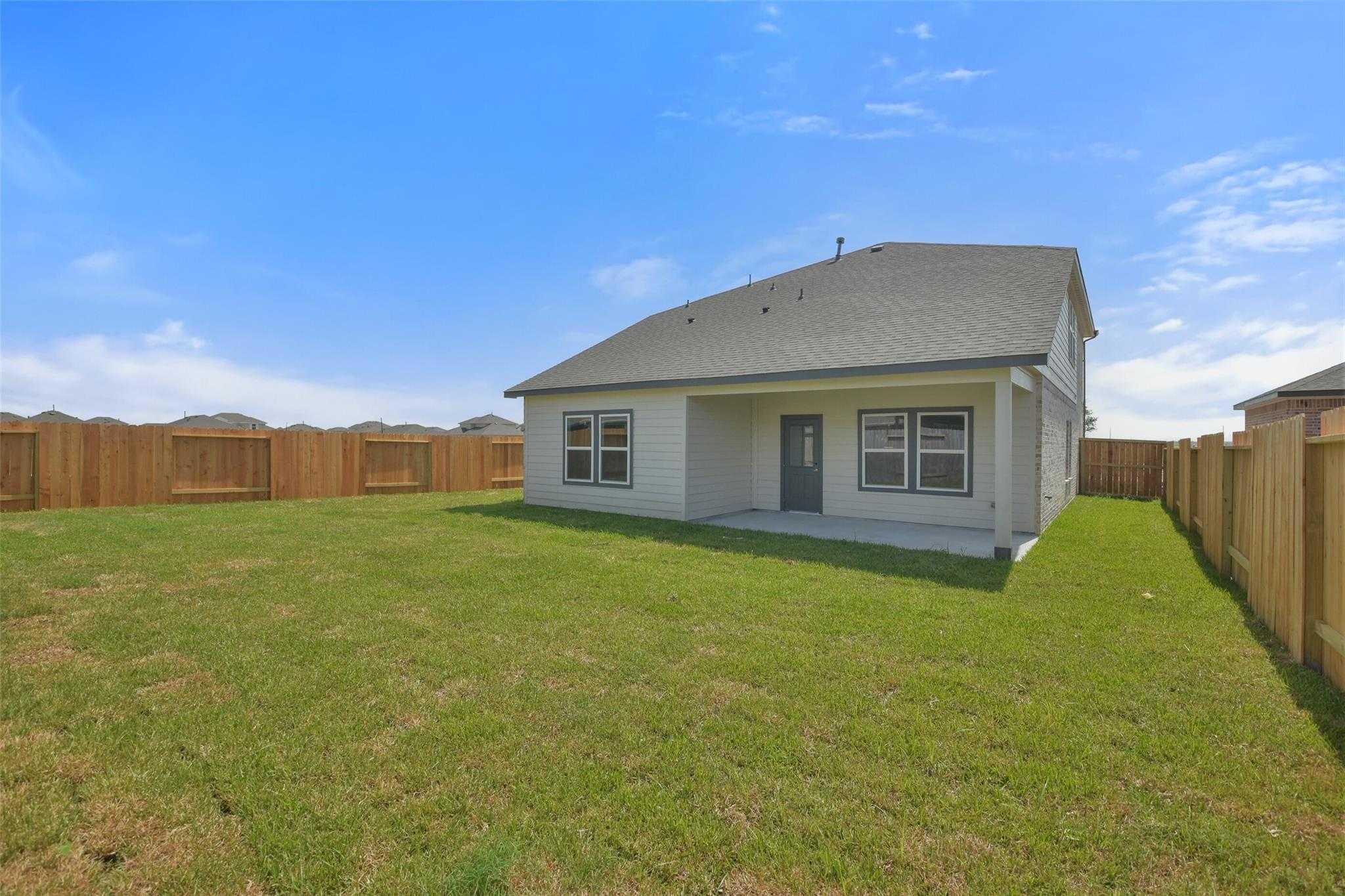 Backyard view of Davidson Homes The Tierra A 4-bedroom home with covered patio, lush green lawn, and wooden privacy fence in River Ranch Meadows, Dayton, Texas