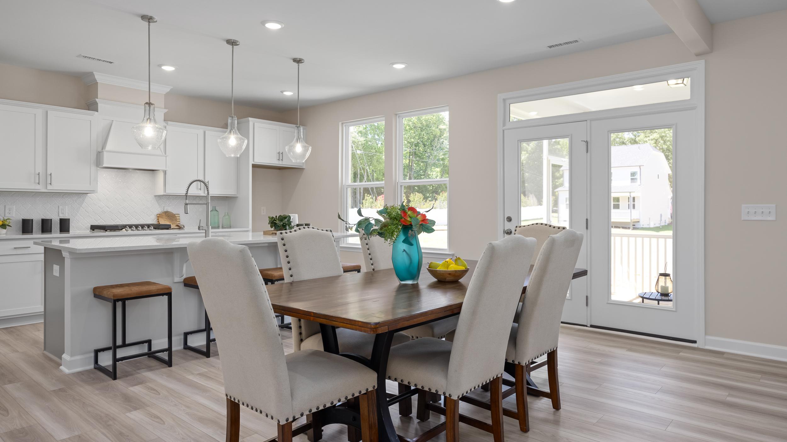 Open-concept kitchen and dining at Stagecoach Corner in Mebane NC with white cabinets, farmhouse island, wooden table, and French doors