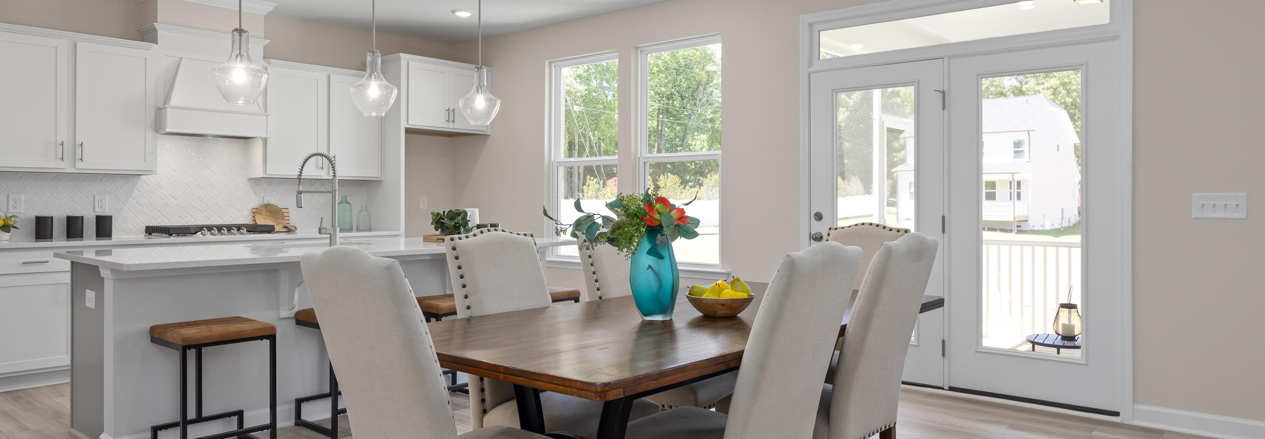 Open-concept kitchen and dining at Stagecoach Corner in Mebane NC with white cabinets, farmhouse island, wooden table, and French doors