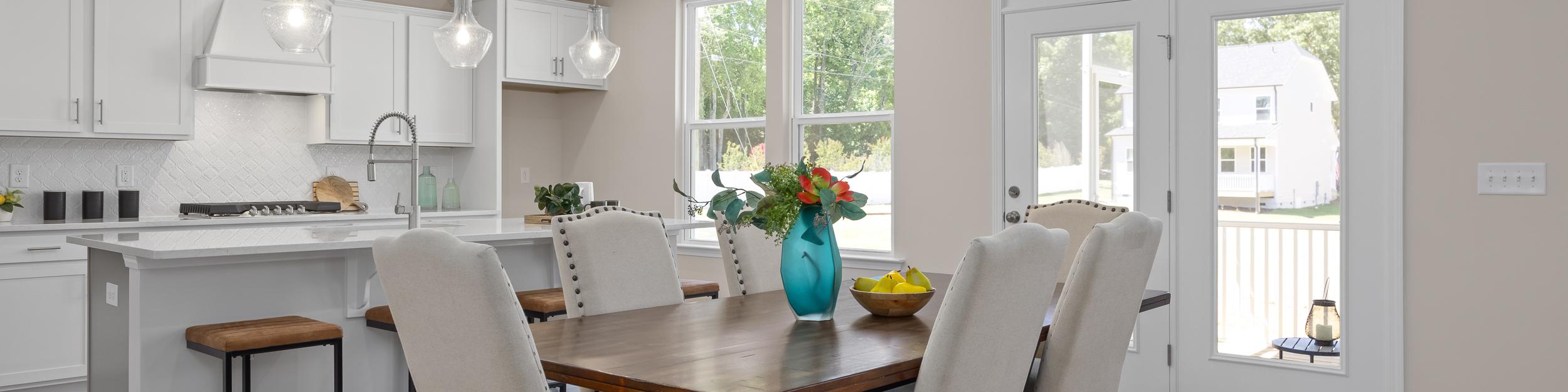 Open-concept kitchen and dining at Stagecoach Corner in Mebane NC with white cabinets, farmhouse island, wooden table, and French doors