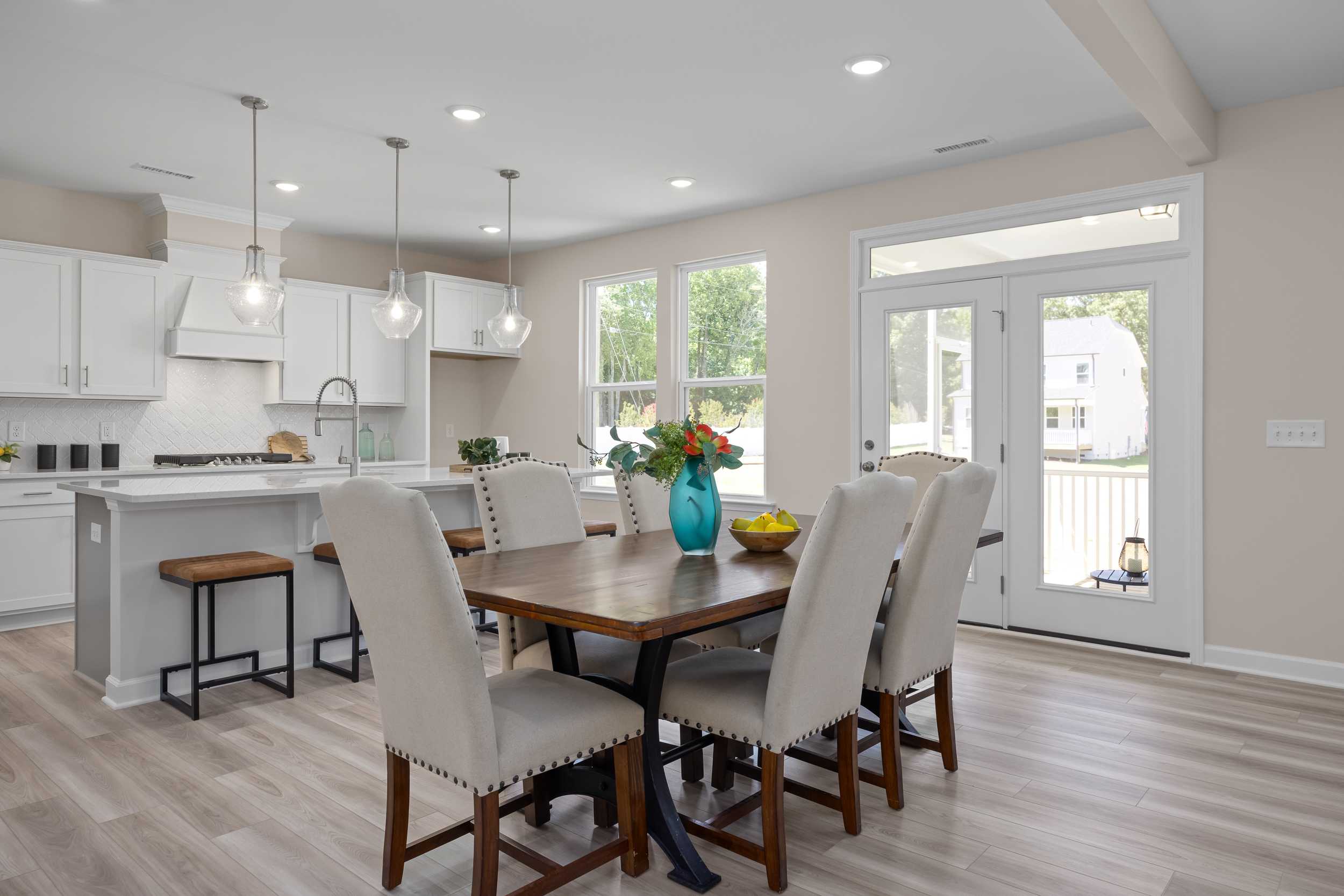Open-concept kitchen and dining at Stagecoach Corner in Mebane NC with white cabinets, farmhouse island, wooden table, and French doors
