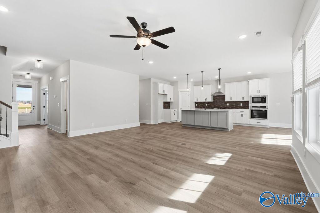 Open-concept kitchen and living space with white cabinets, gray island, pendant lights, and hardwood floors in Davidson Homes The Rockford, Hartselle, Alabama