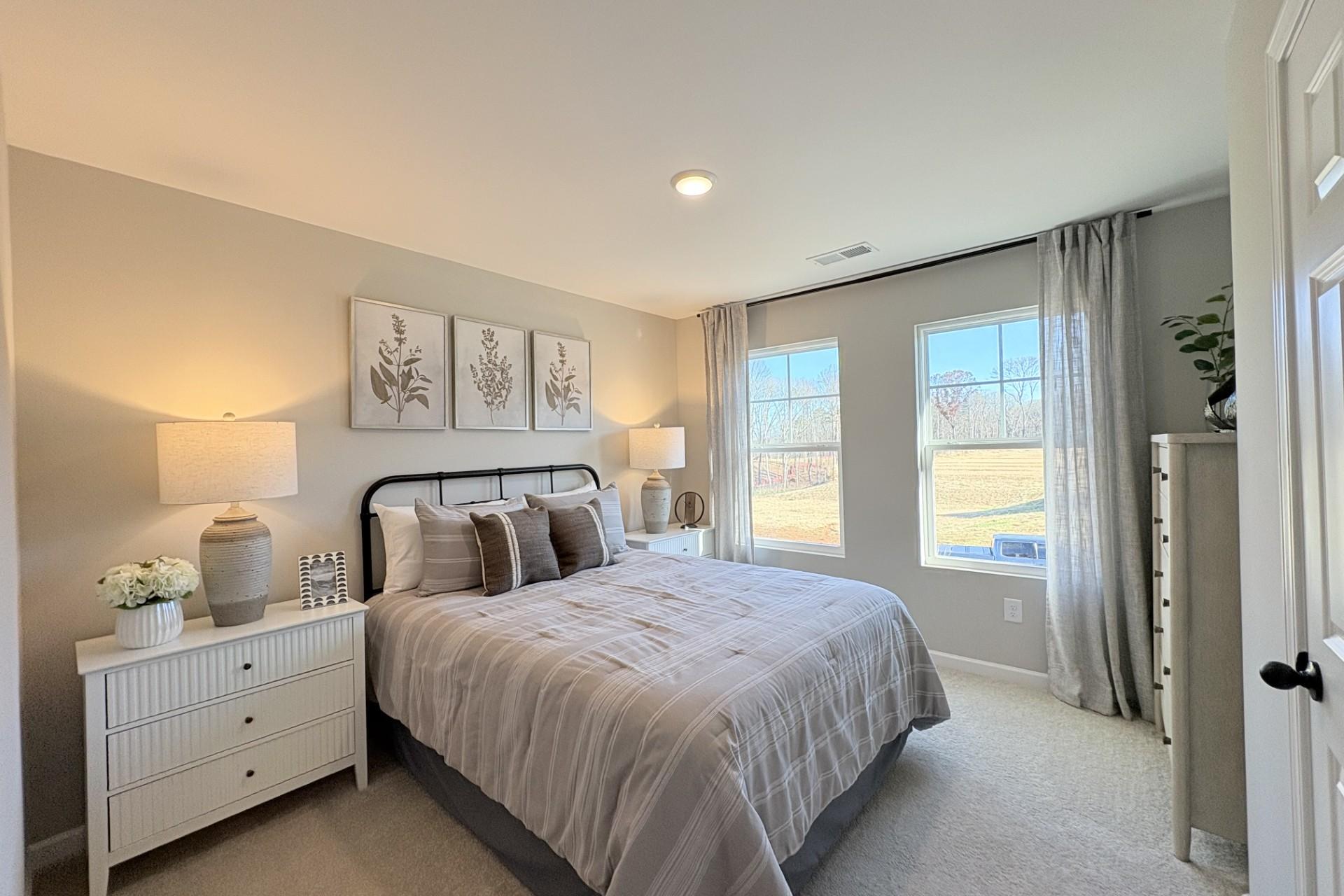 Serene primary bedroom in Hemingway community, Cumming Georgia by Davidson Homes with neutral bedding, large windows and botanical art