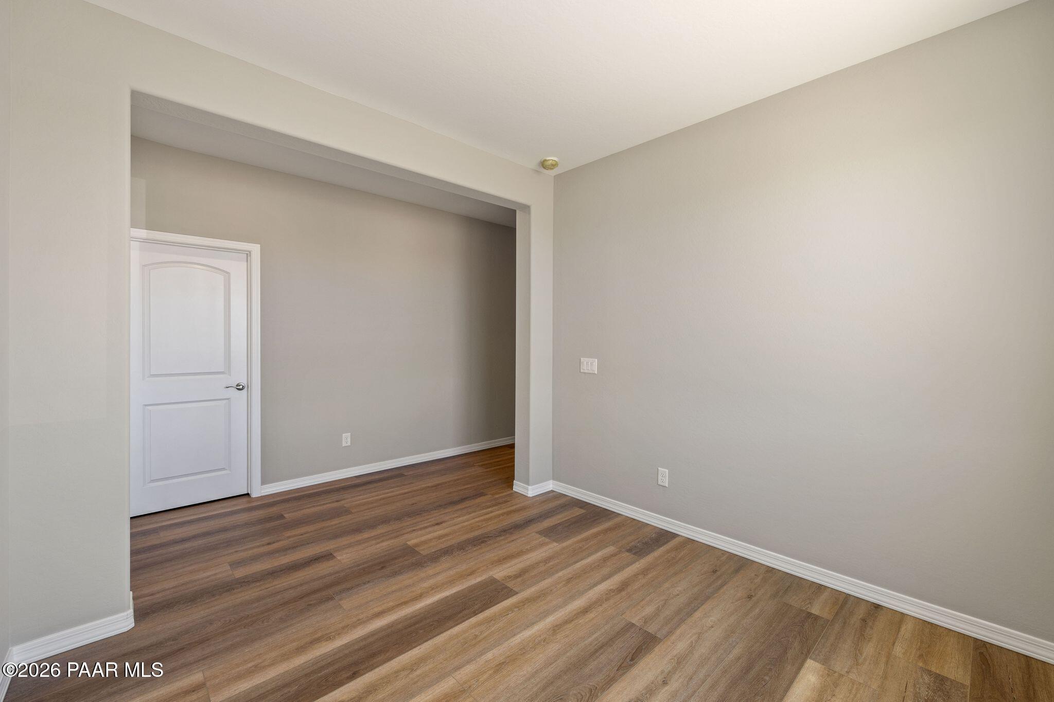 Spacious bedroom with light gray walls, warm hardwood floors, white closet door, and arched entry in Davidson Homes The Frontier A, Prescott Valley, AZ