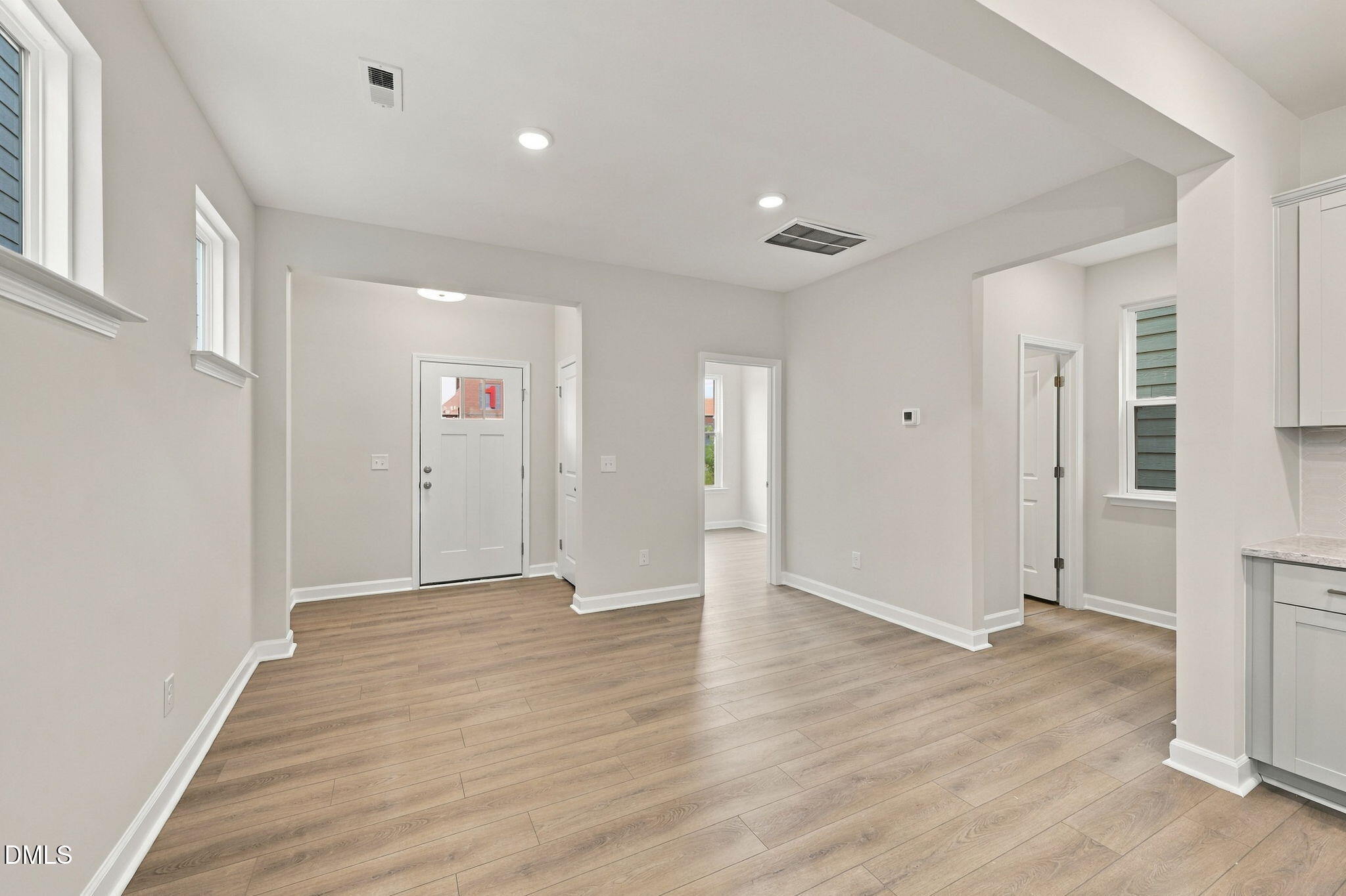 Open-concept living area with luxury vinyl plank flooring and white front door in The Alexander B floor plan, Knightdale NC
