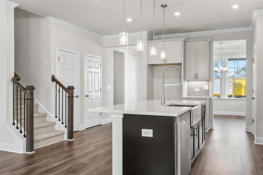 Modern open-concept kitchen with white cabinets, large island sink, pendant lights, and wood staircase in The Ash C at Wehunt Meadows, Hoschton