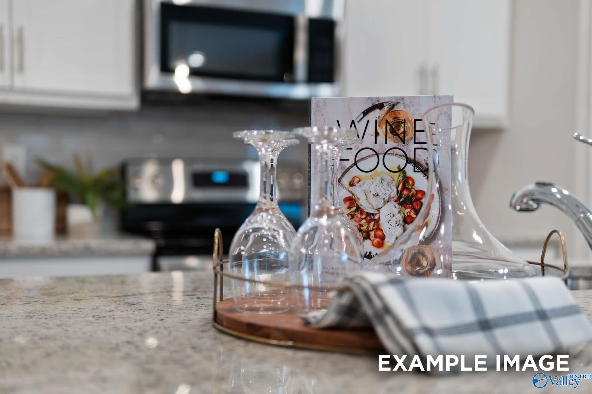 Granite countertop with wine glasses and serving tray in modern kitchen at The Camilla C by Davidson Homes, Hartselle, Alabama