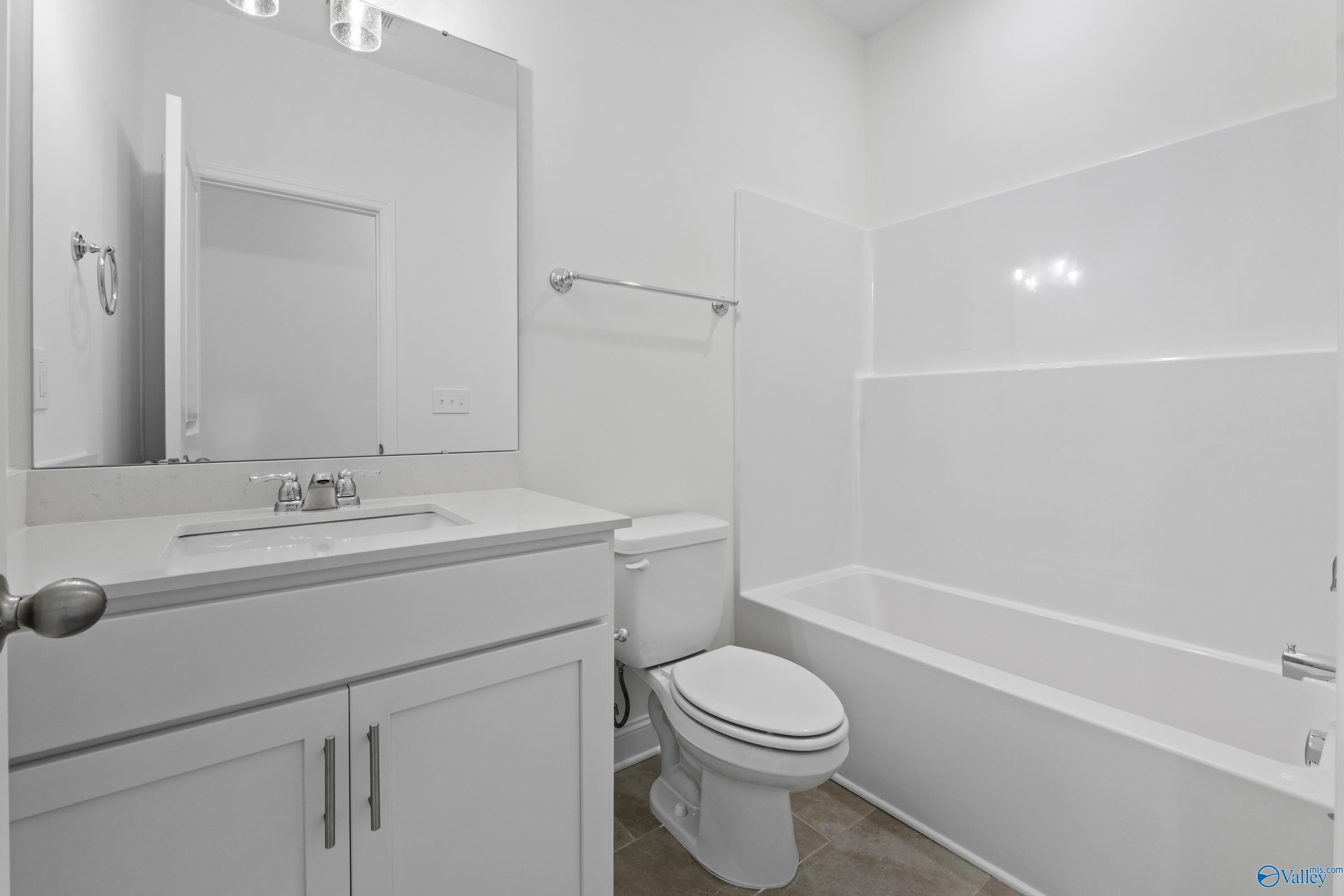 Bright white bathroom with bathtub, vanity sink, toilet, and large mirror in Davidson Homes The Rockford B, Toney, Alabama