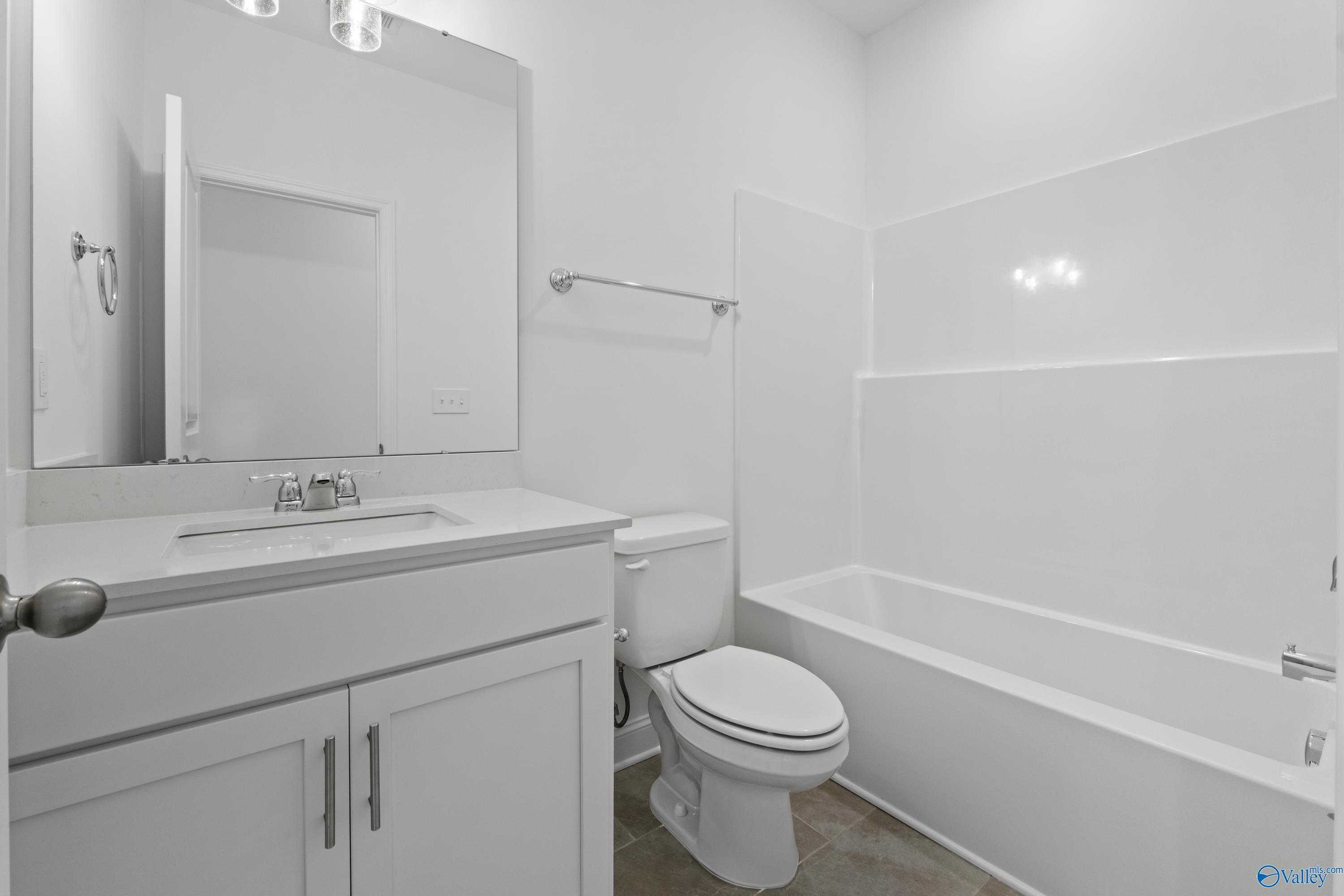 Bright white bathroom with bathtub, vanity sink, toilet, and large mirror in Davidson Homes The Rockford B, Toney, Alabama