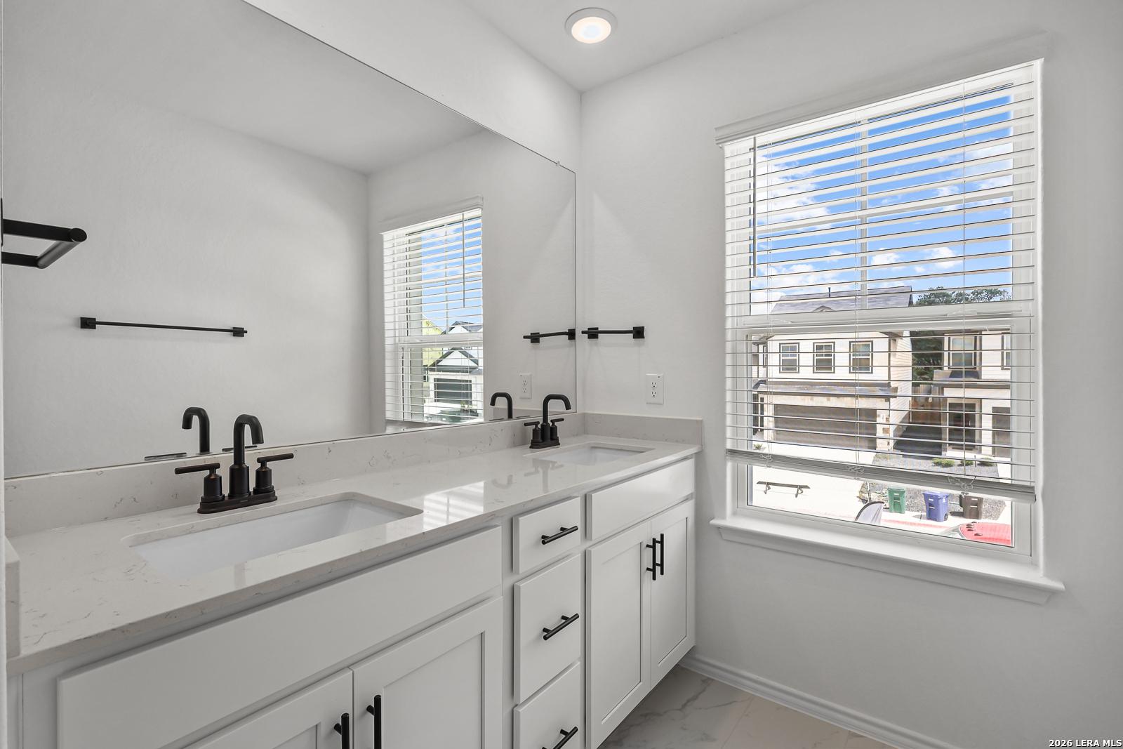 Modern bathroom with double vanity, quartz countertops, and matte black fixtures in The Gillian C home, San Antonio, Texas.