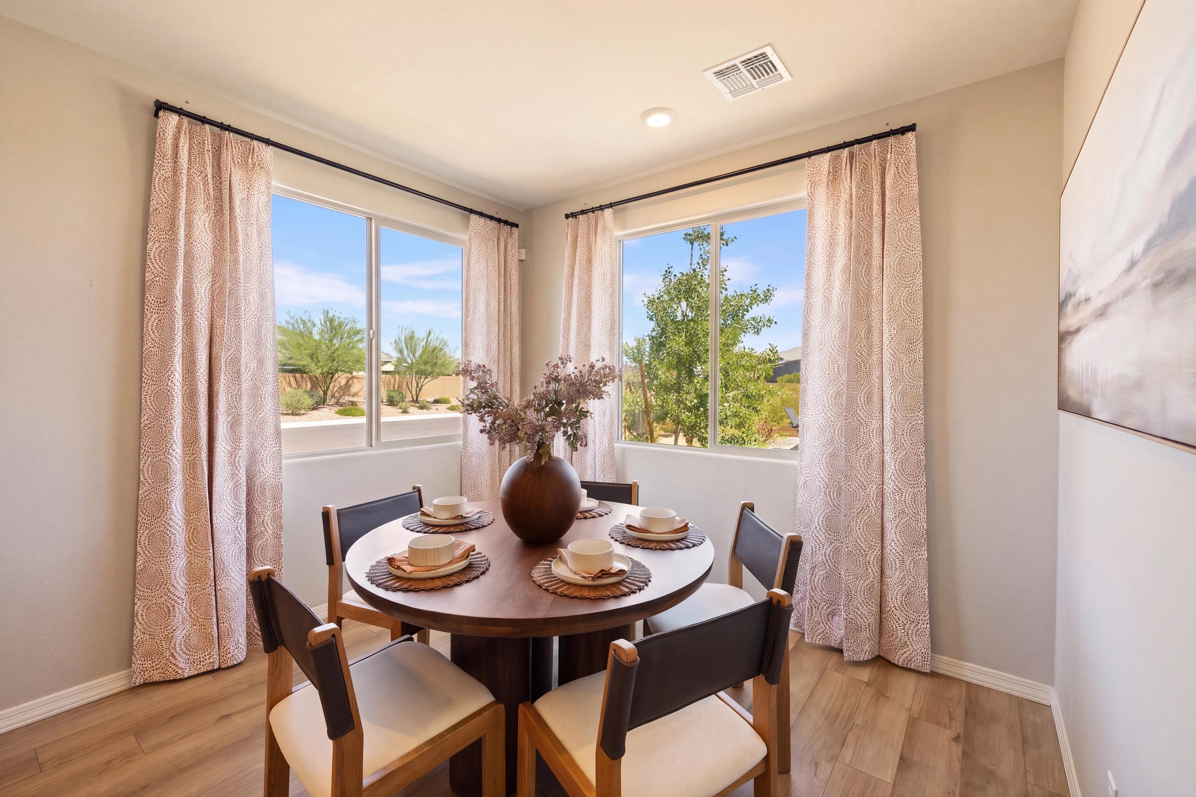 Bright dining nook with round wood table, corner windows, and patterned curtains at North Ridge at Pronghorn Ranch by Davidson Homes, Prescott Valley AZ