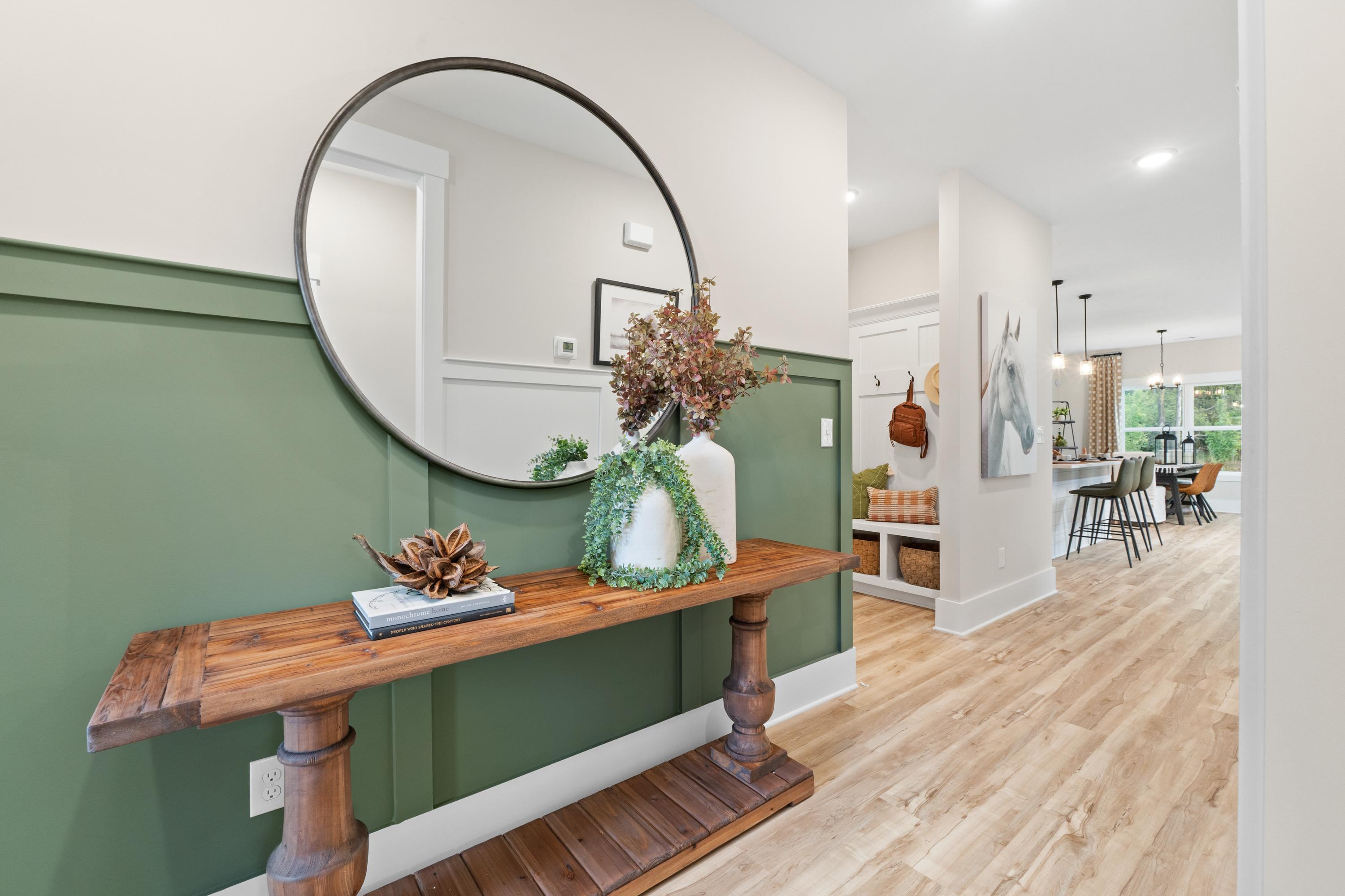 Spacious entryway in Spragins Cove Huntsville AL with wooden console table, round mirror, sage green wall and potted greenery