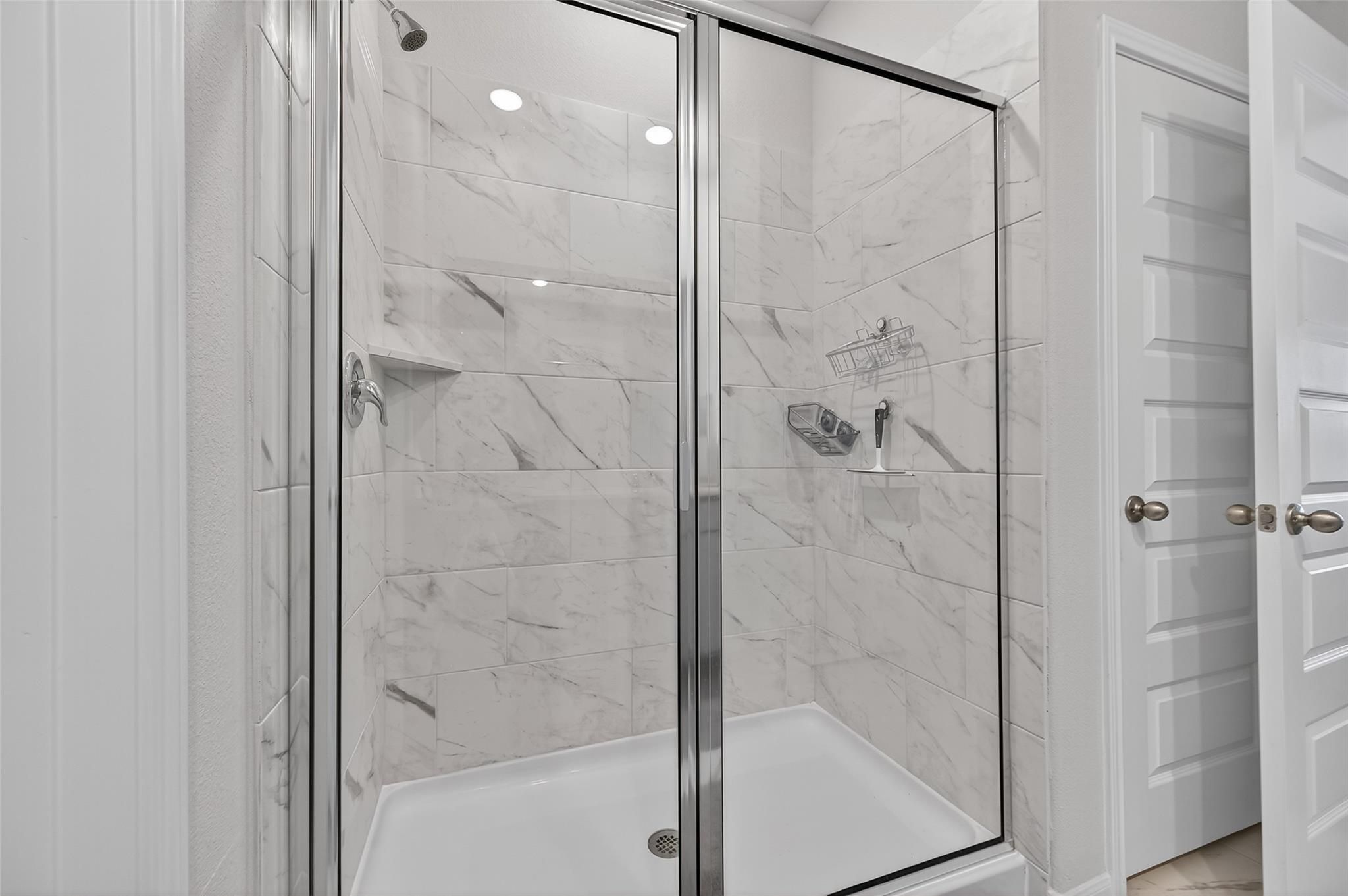 Elegant frameless glass shower with white subway tile walls and built-in shelves in master bath of Davidson Homes The Brazos E, Magnolia TX
