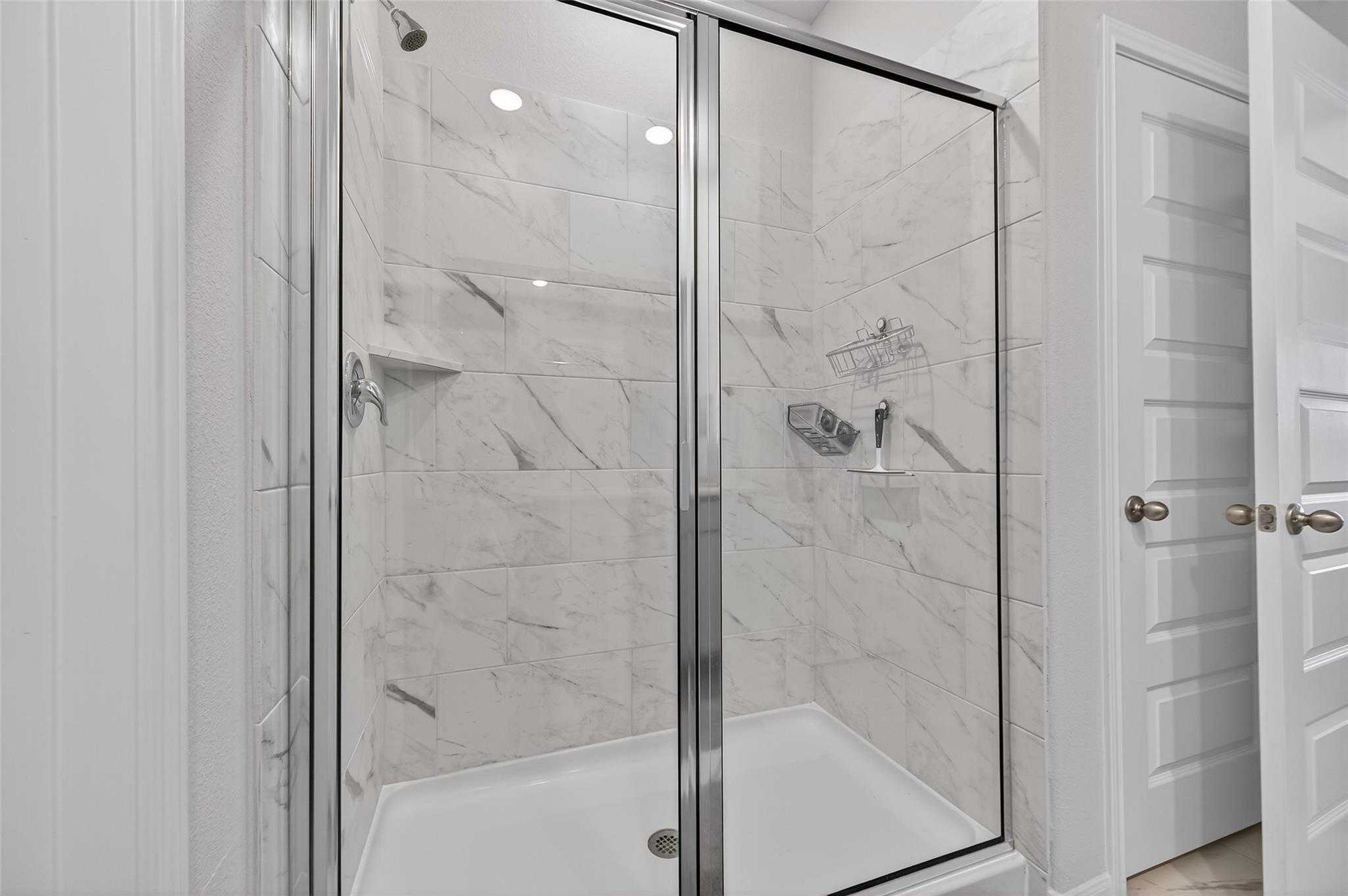 Elegant frameless glass shower with white subway tile walls and built-in shelves in master bath of Davidson Homes The Brazos E, Magnolia TX