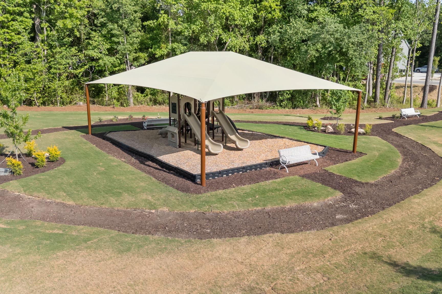 Community playground at Wendell Ridge in Wendell, NC with shaded play equipment, mulched ground, and park benches.