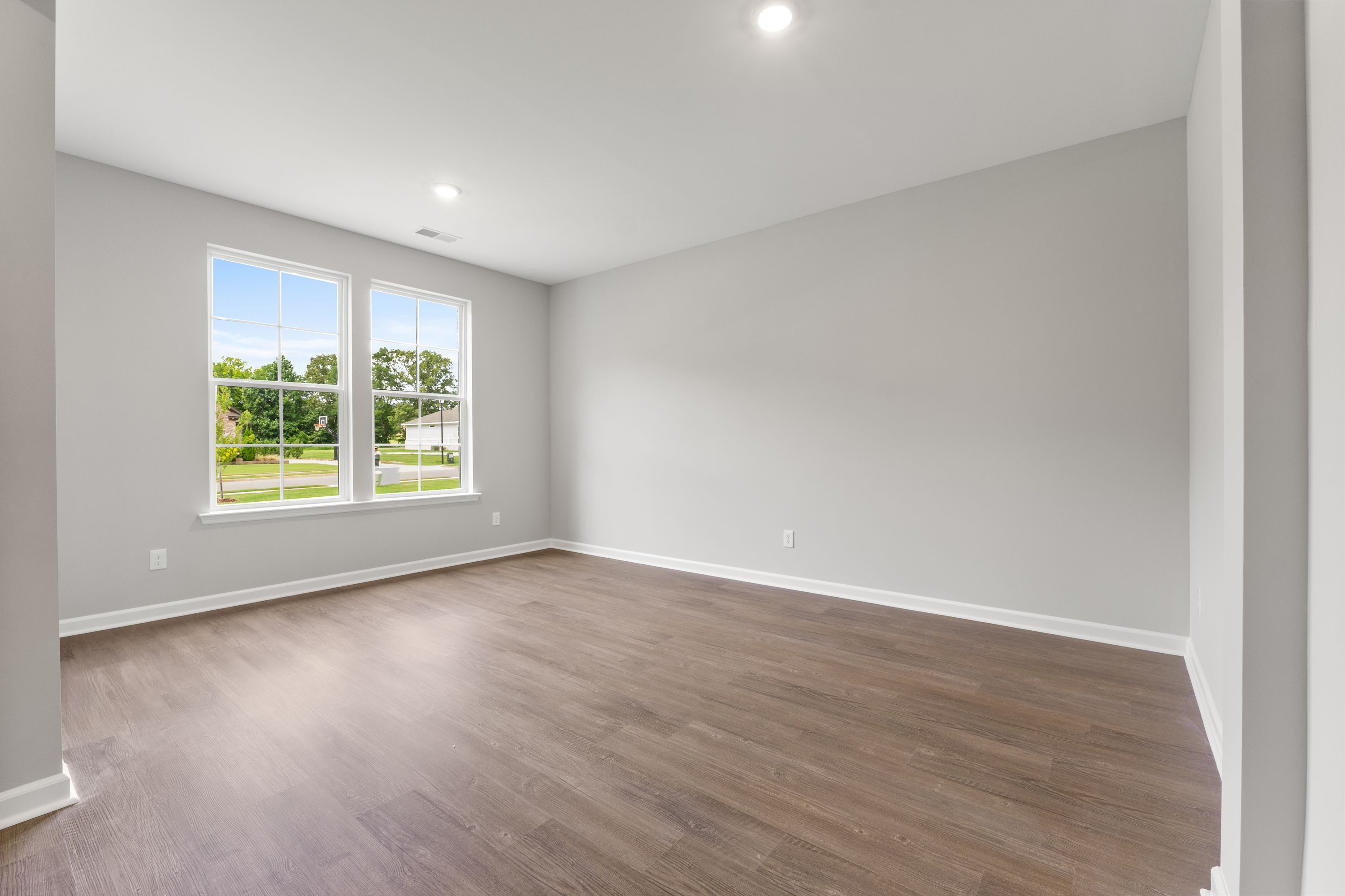 Spacious master suite in The Avalon E with light gray walls, large windows overlooking lawn, hardwood floors