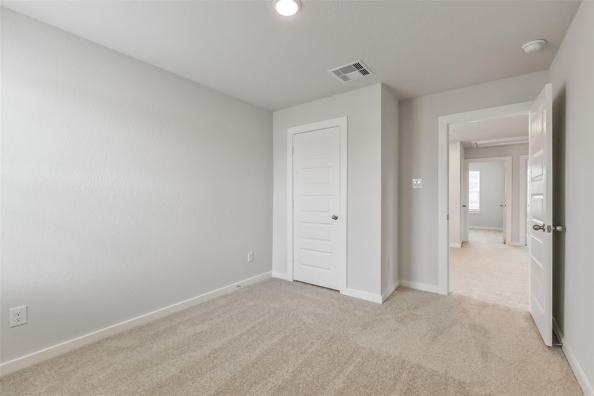 Spacious secondary bedroom with light gray walls, beige carpet, and open door in The Brazos E by Davidson Homes, Cleveland, TX