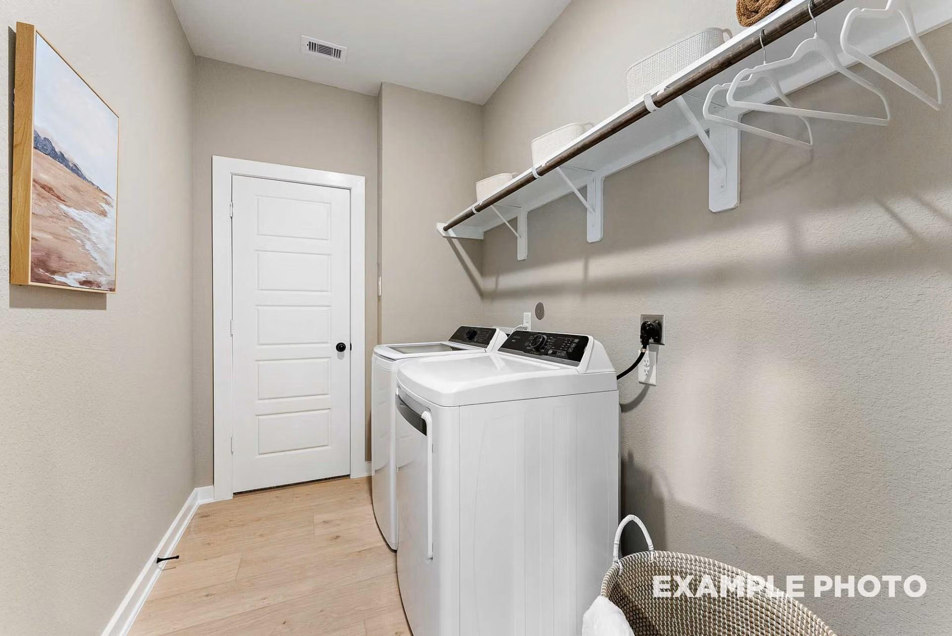 Spacious laundry room with white washer dryer, wooden shelves, hanging rods and beige walls in Davidson Homes The Everett C, Dayton Texas