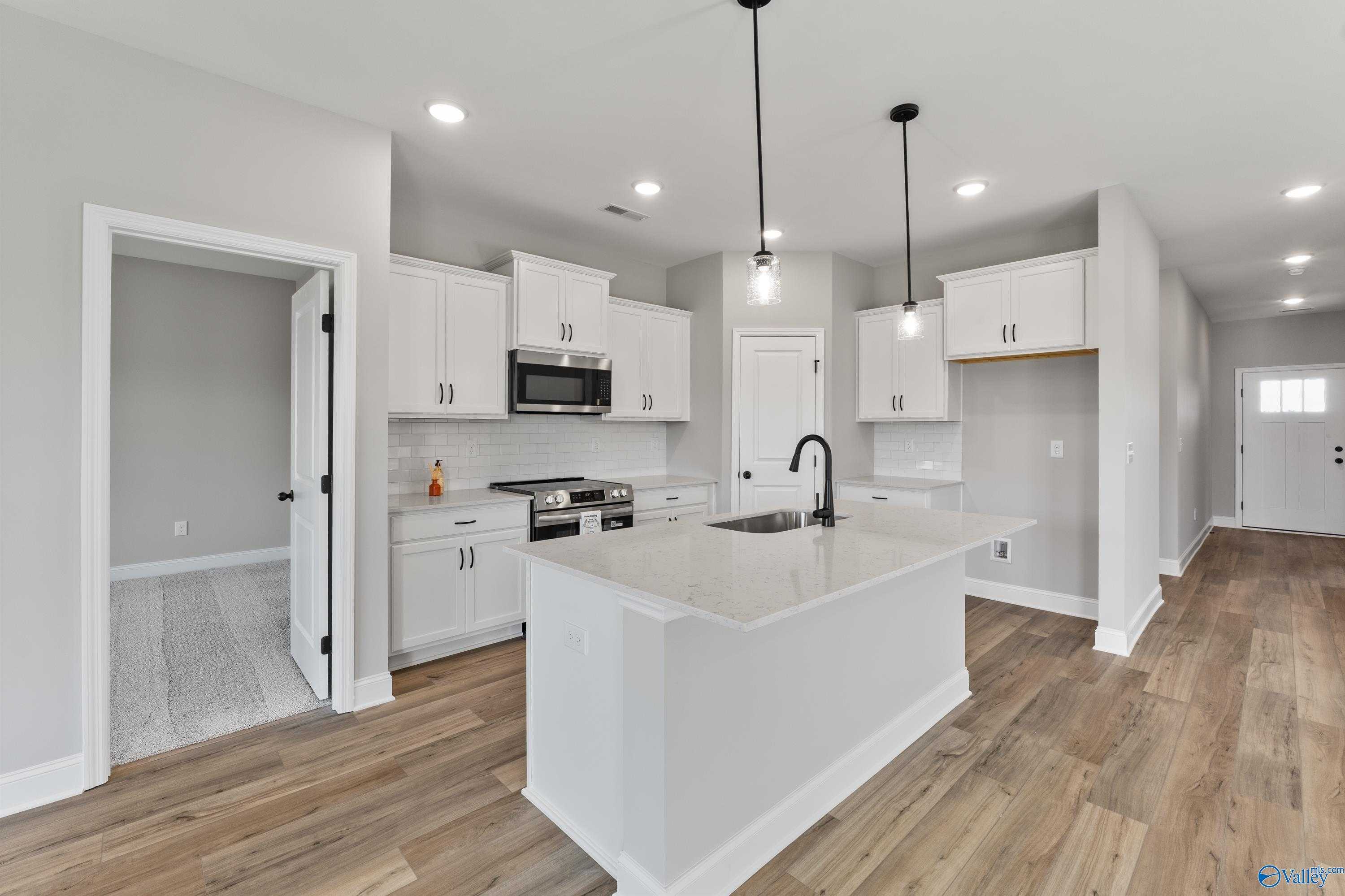 Modern white kitchen featuring large quartz island, stainless steel appliances, and open layout in Davidson Homes The Franklin B, Hazel Green, AL
